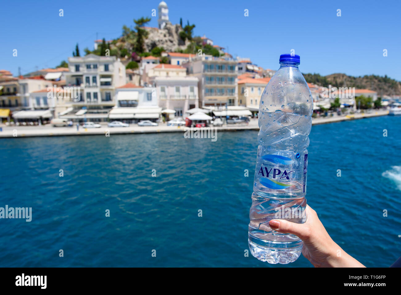 16.06.2016. POROS ISLAND, GREECE.  A bottle of plastic AYPA mineralwater in hands. Poros island at background. Cruise with ferry. Stock Photo