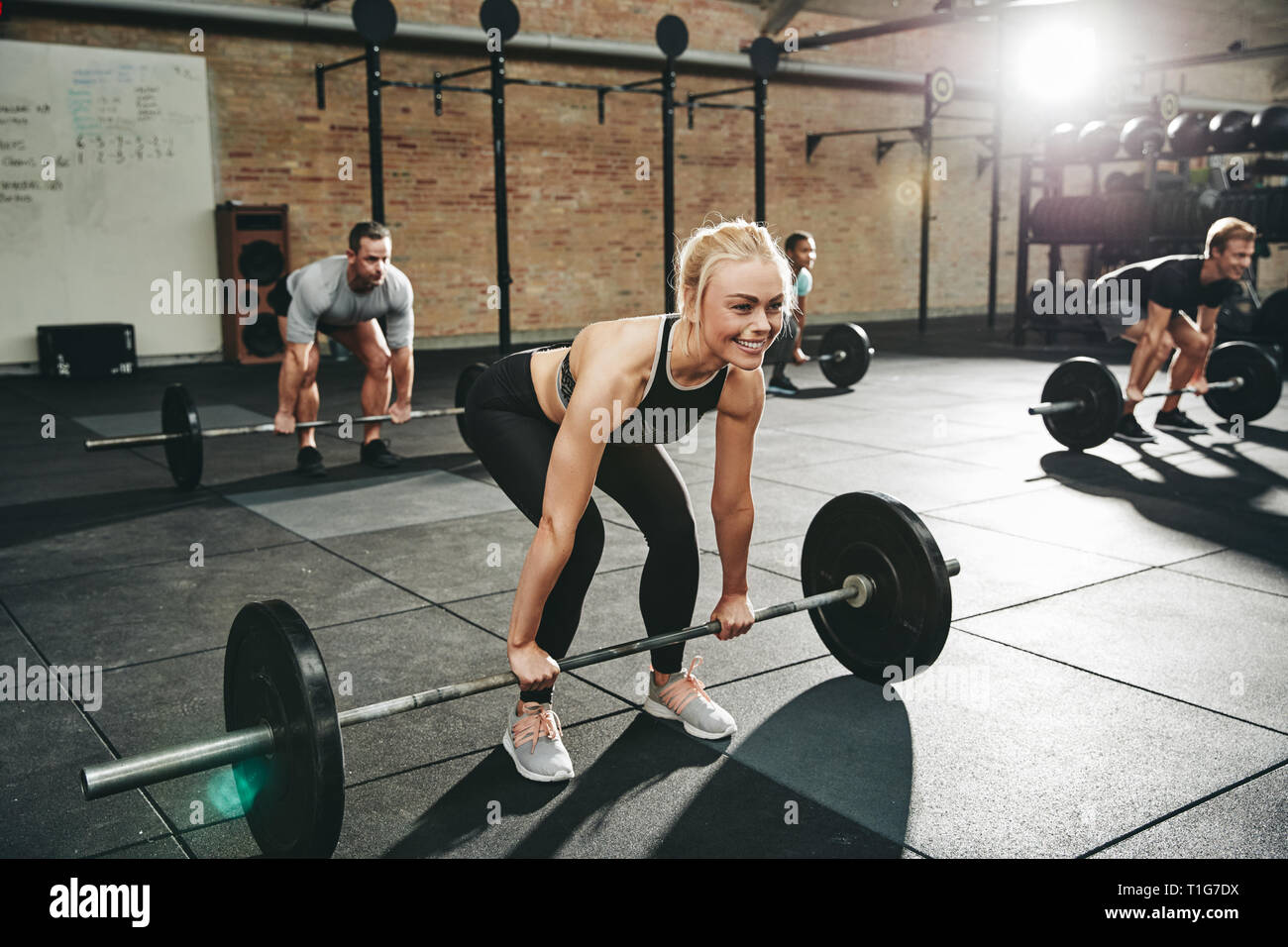 Fit young woman in sportswear smiling while lifting barbells during a ...
