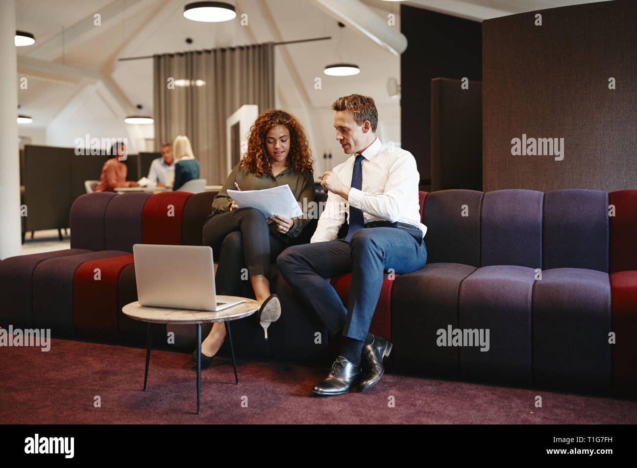 Two diverse business colleagues sitting on a sofa in a modern office ...