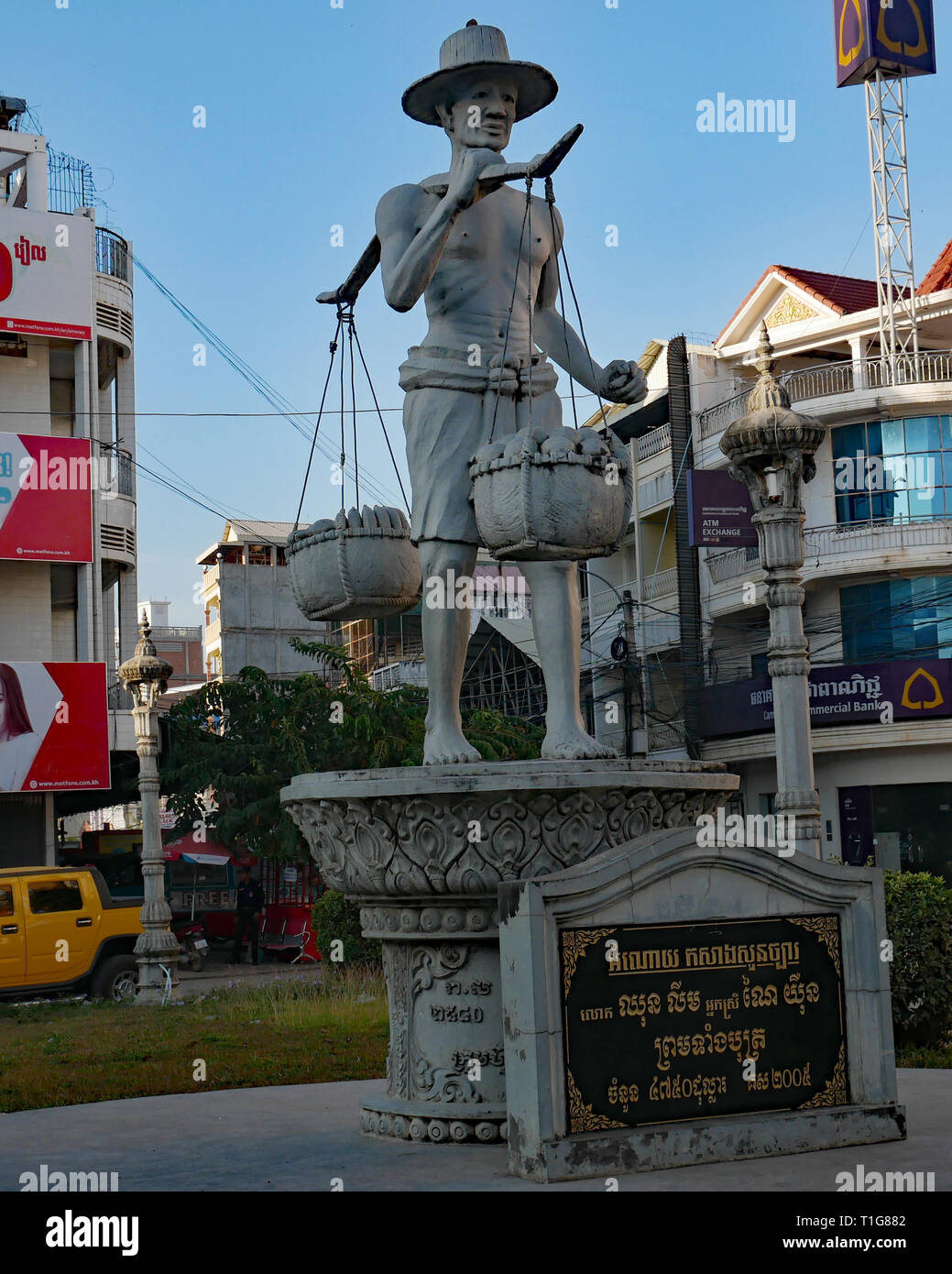 The Peddler Statue is of a man with a yoke across his shoulders, carrying baskets of fruit for sale representing commerce in Battambang city. Stock Photo