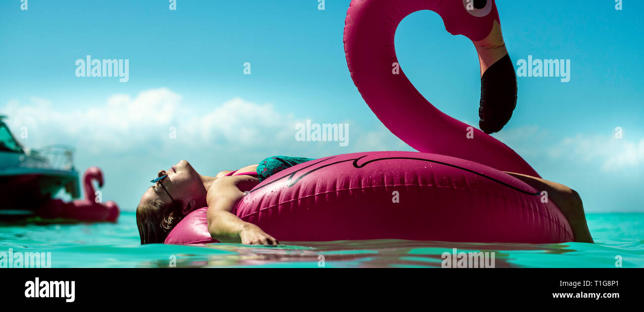Young woman resting for a tan in inflatable flamingo at a sunny day at sea with yatchs on the horizon. Stock Photo