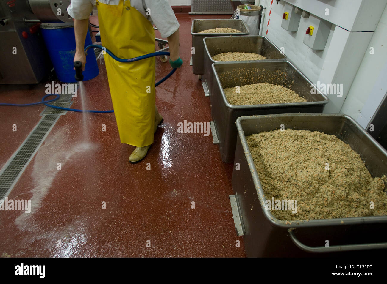 A worker in protective clothing cleaning the floors next to trays of