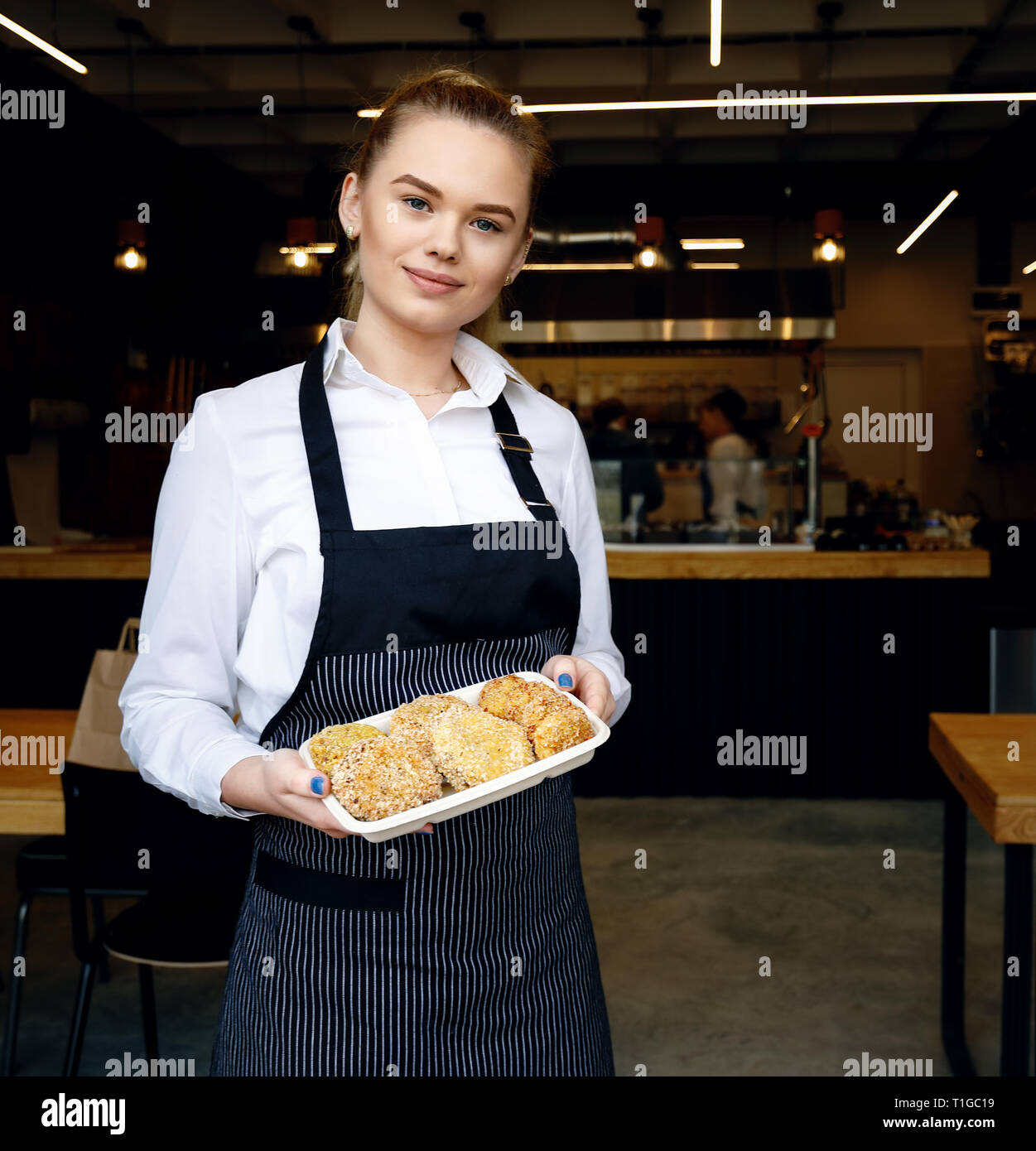 Friendly waitress welcoming customers at restaurant door. Adult young woman greeting customers and inviting to taste meatballs. Small family restauran Stock Photo
