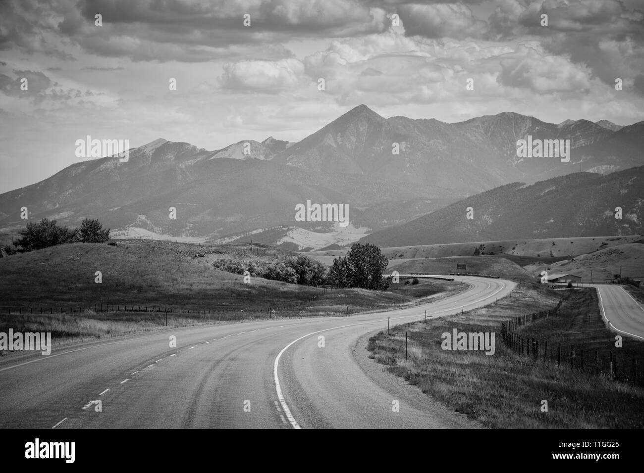 A sweeping and serene view of a Montana mountain range with a  meadow in foreground with an interstate highway winding towards the horizon in MT Stock Photo