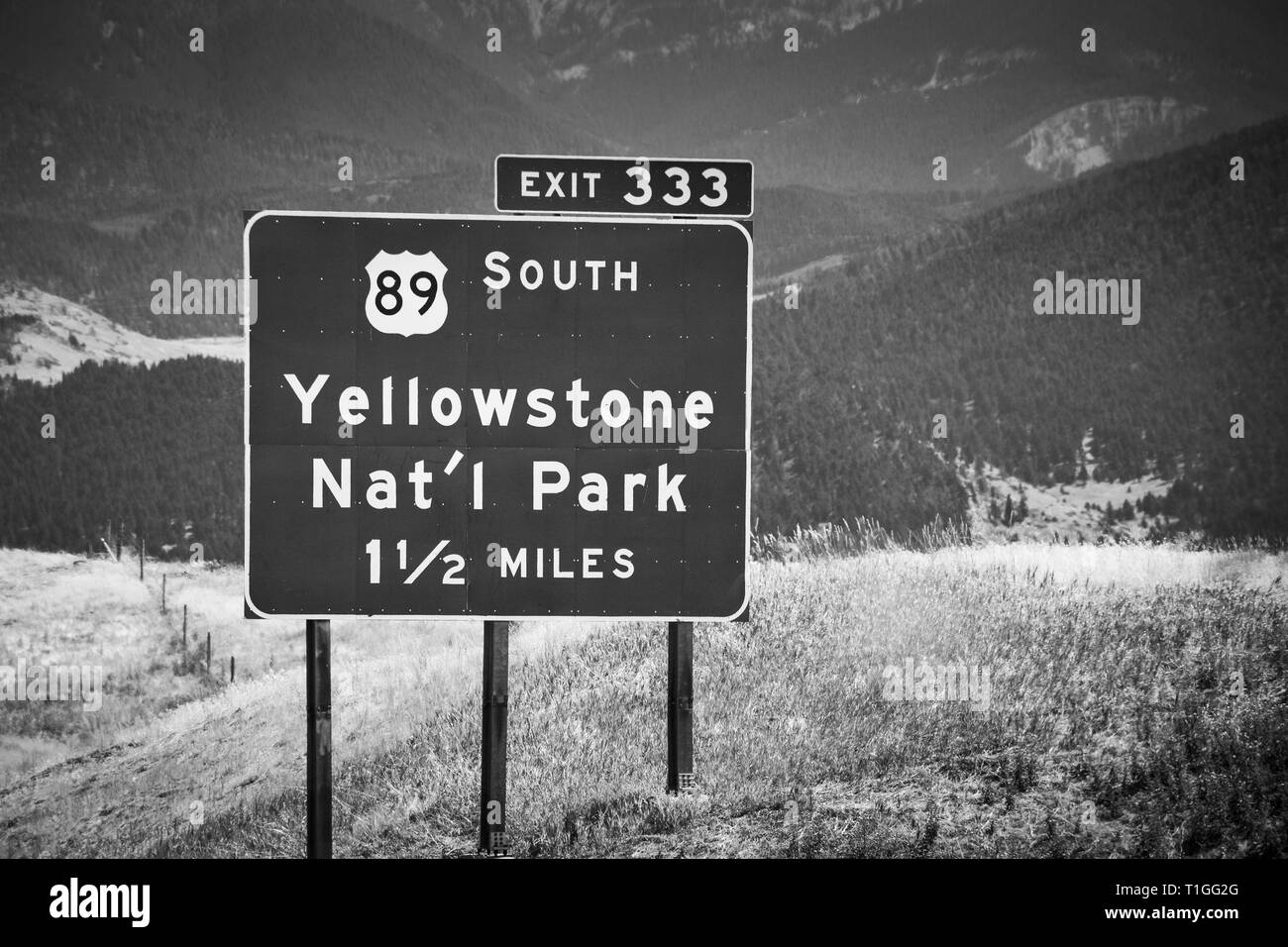 A Montana inerstate exit sign for Yellowstone National Park,  with mountian backdrop on I-90 in black and white Stock Photo
