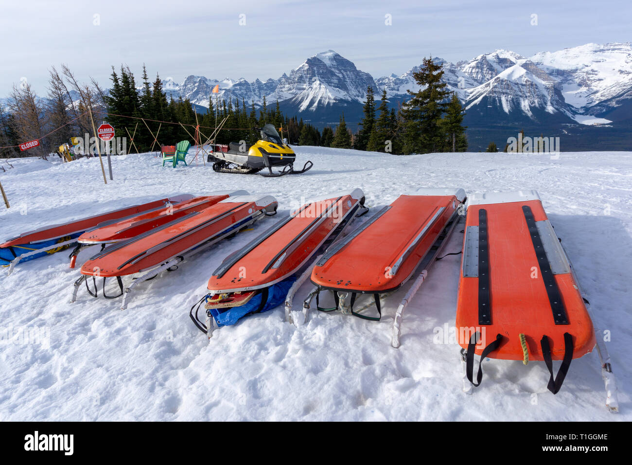 Rows of ski patrol toboggans or rescue sleds lie on snow on mountain