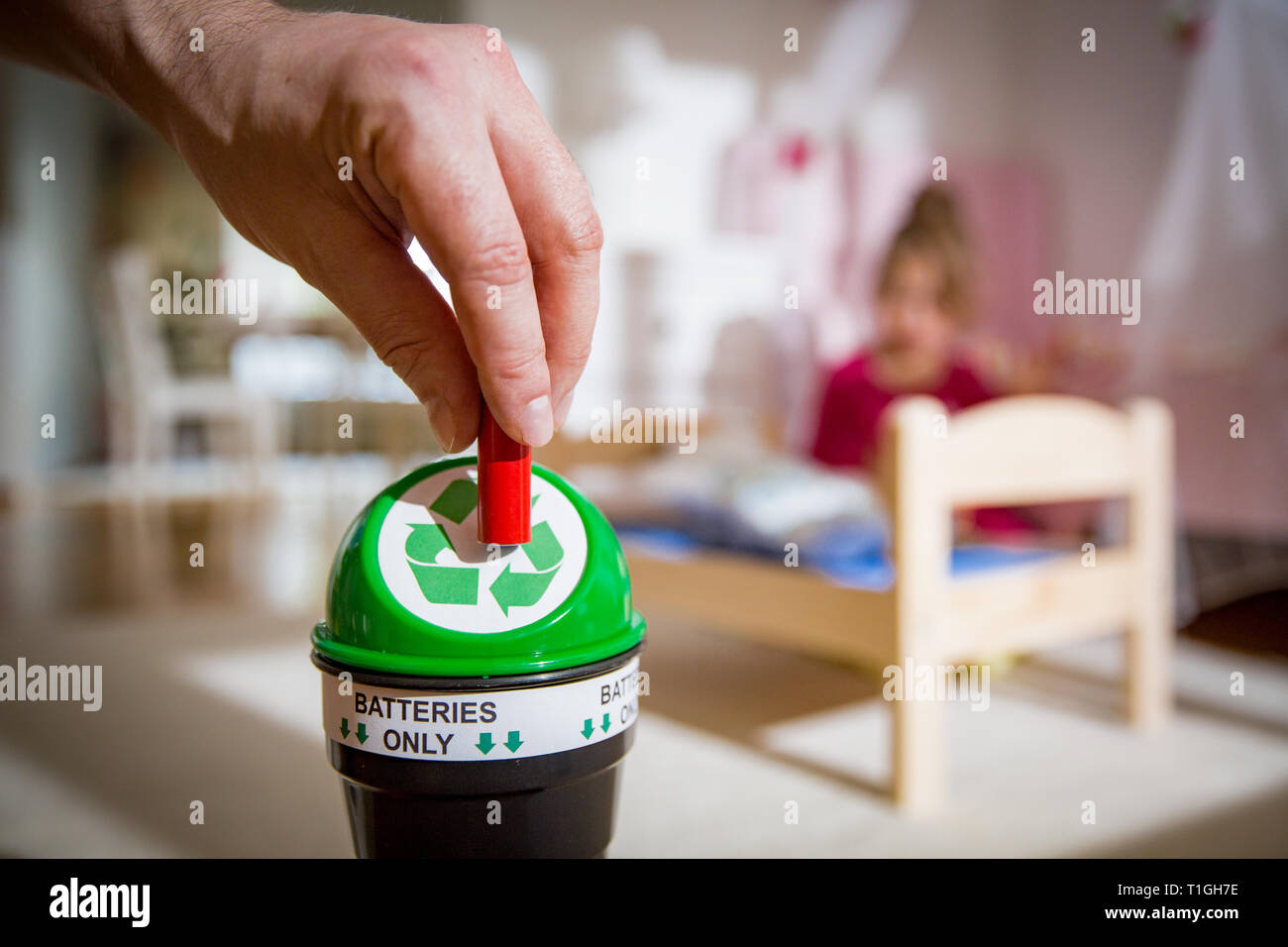 Man putting used batteries into recycling box at home. Child in the nursery room playing with toys. Separating waste concept. Batteries Only. Stock Photo