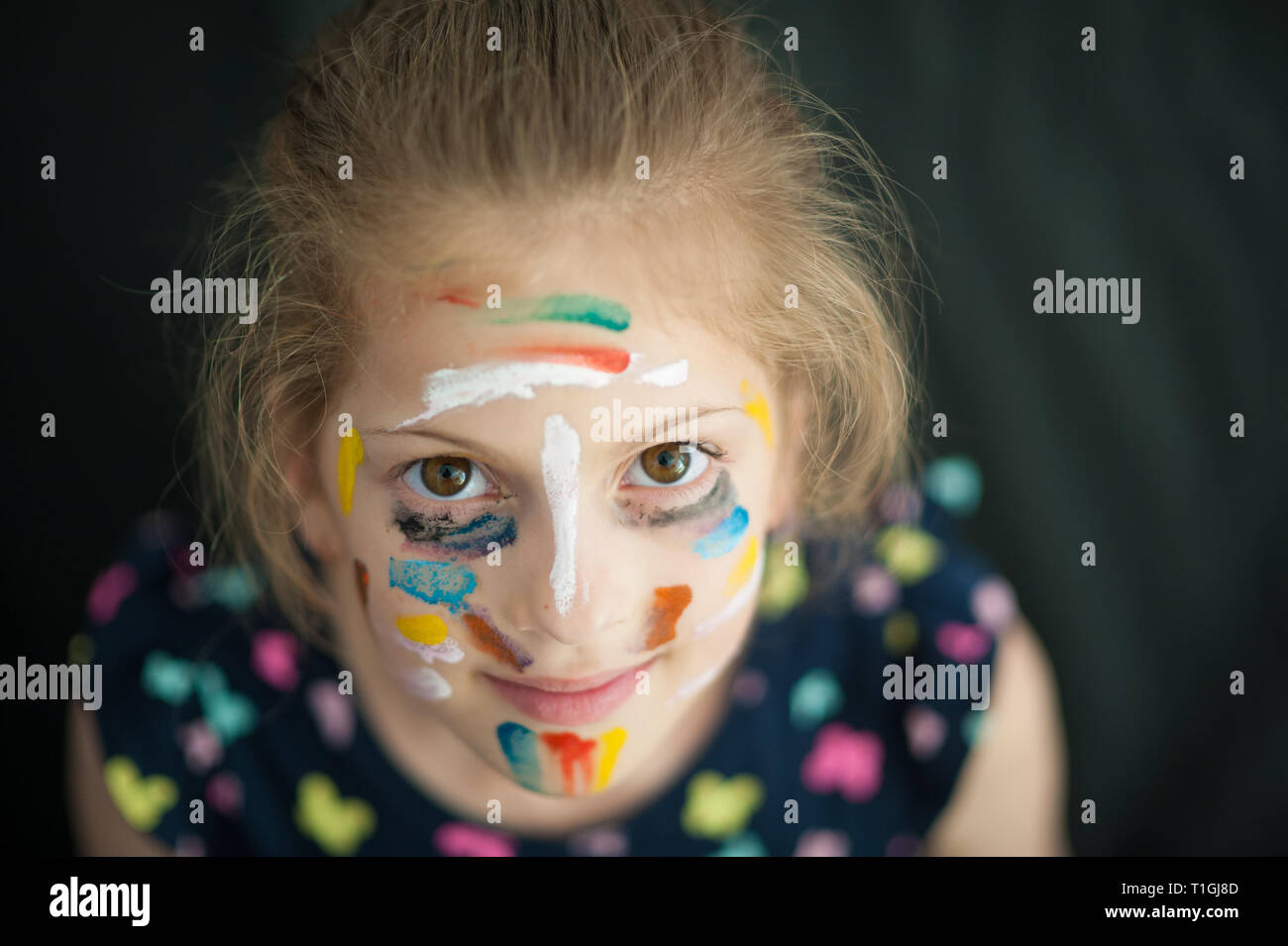 pretty little caucasian girl in multicolored dress with painted colorful face smiling Stock Photo