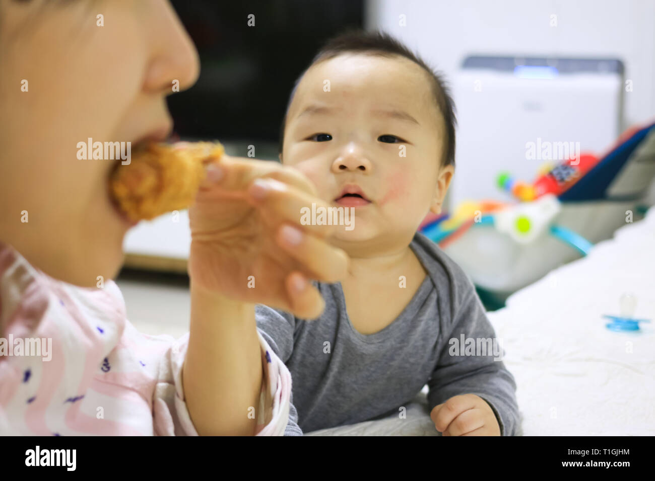 Korean baby seeing mother eating fried chicken with an envious eye