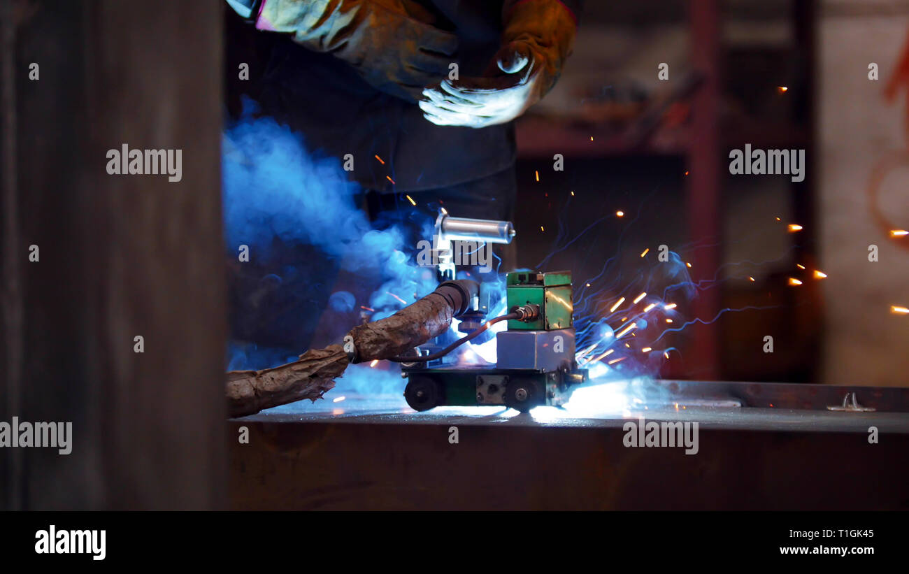 A construction process. A man at the construction plant using a welding machine. Bright blue lighting Stock Photo
