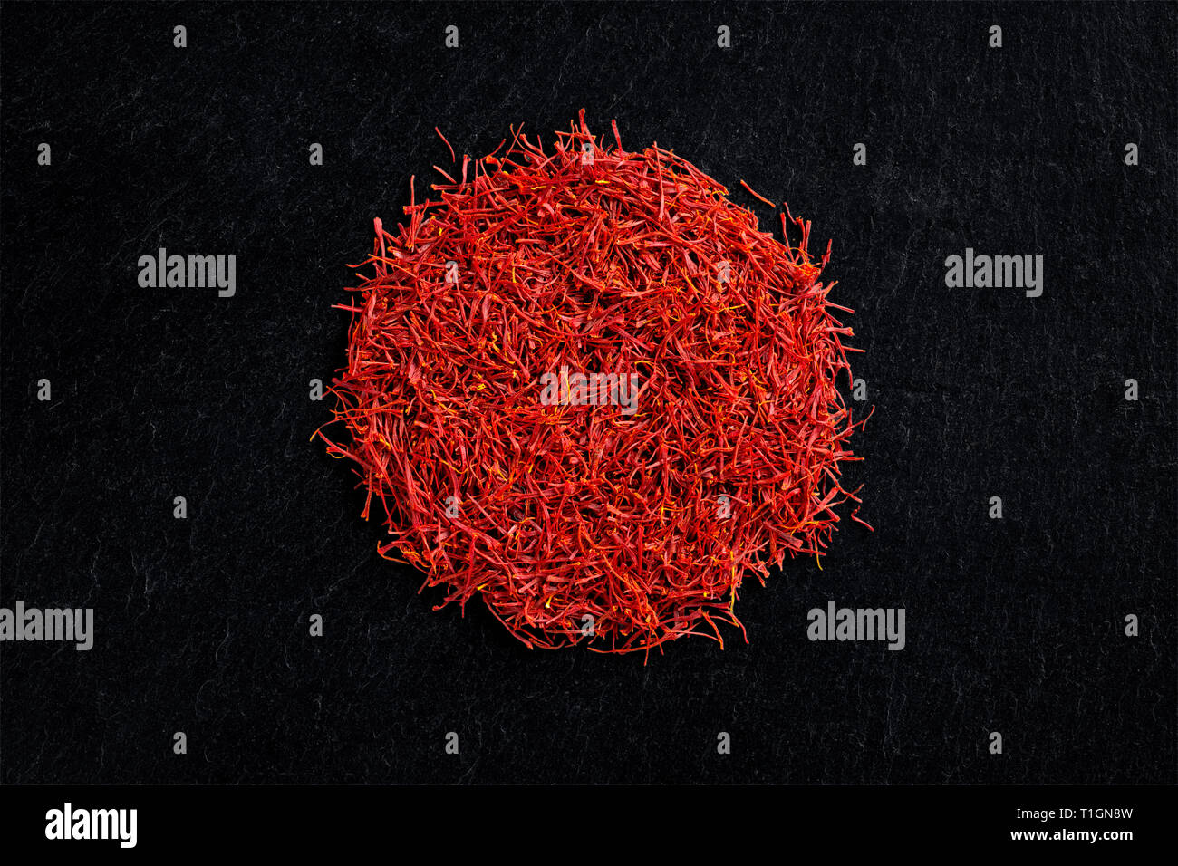 Circular heap of saffron crocus threads on black slate background, view