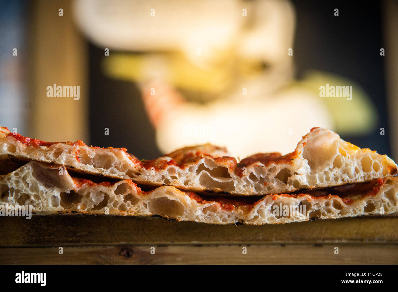 close up of Italian roman style pizza slices showing air bubbles and light crispy base. Selective focus with pulcinella cartoon blurred. Pizza romana Stock Photo