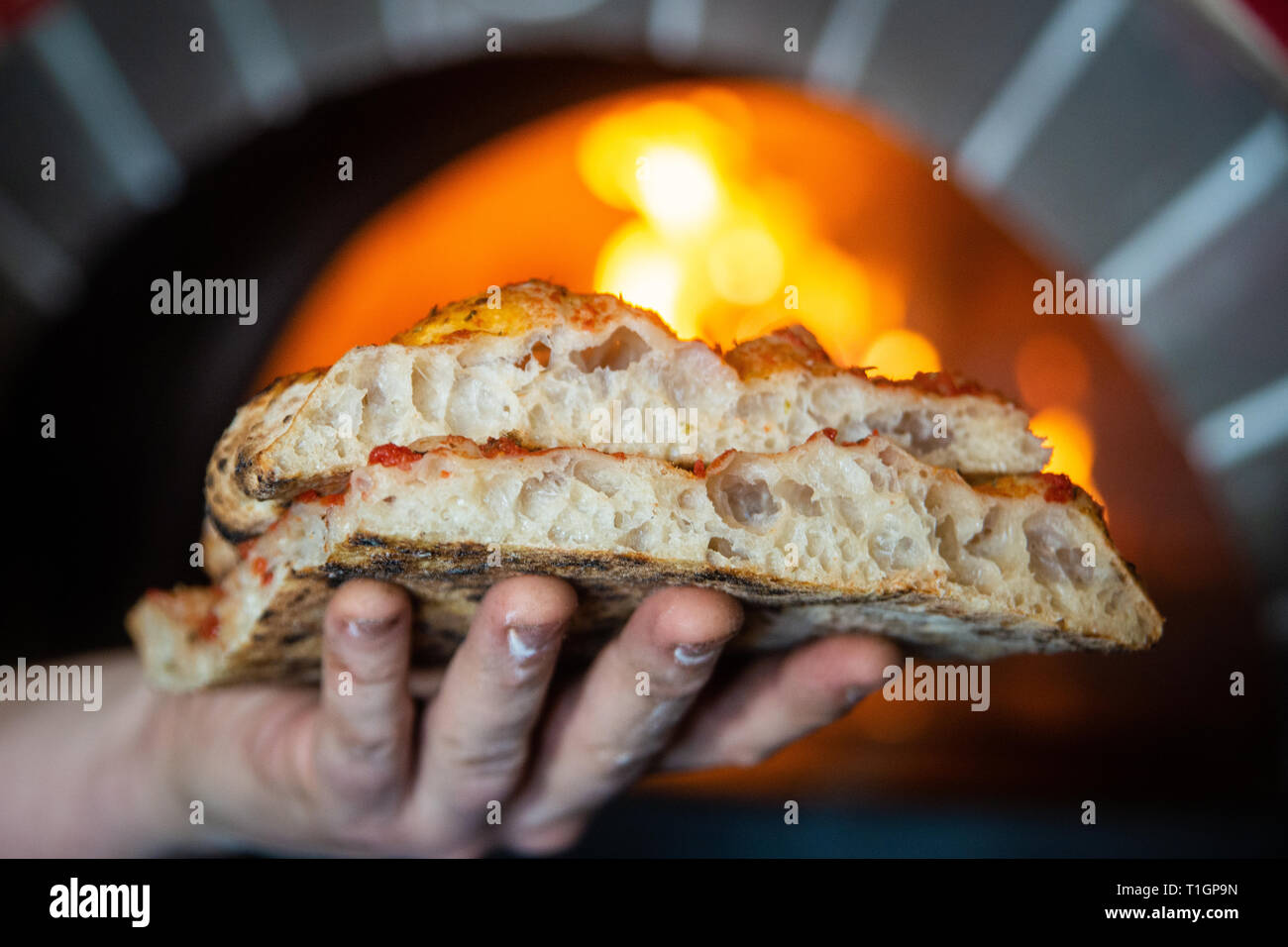 man/chef holding traditional roman Italian style wood fired pizza slices in front of a wood fired oven in a pizzeria/trattoria/restaurant. Stock Photo