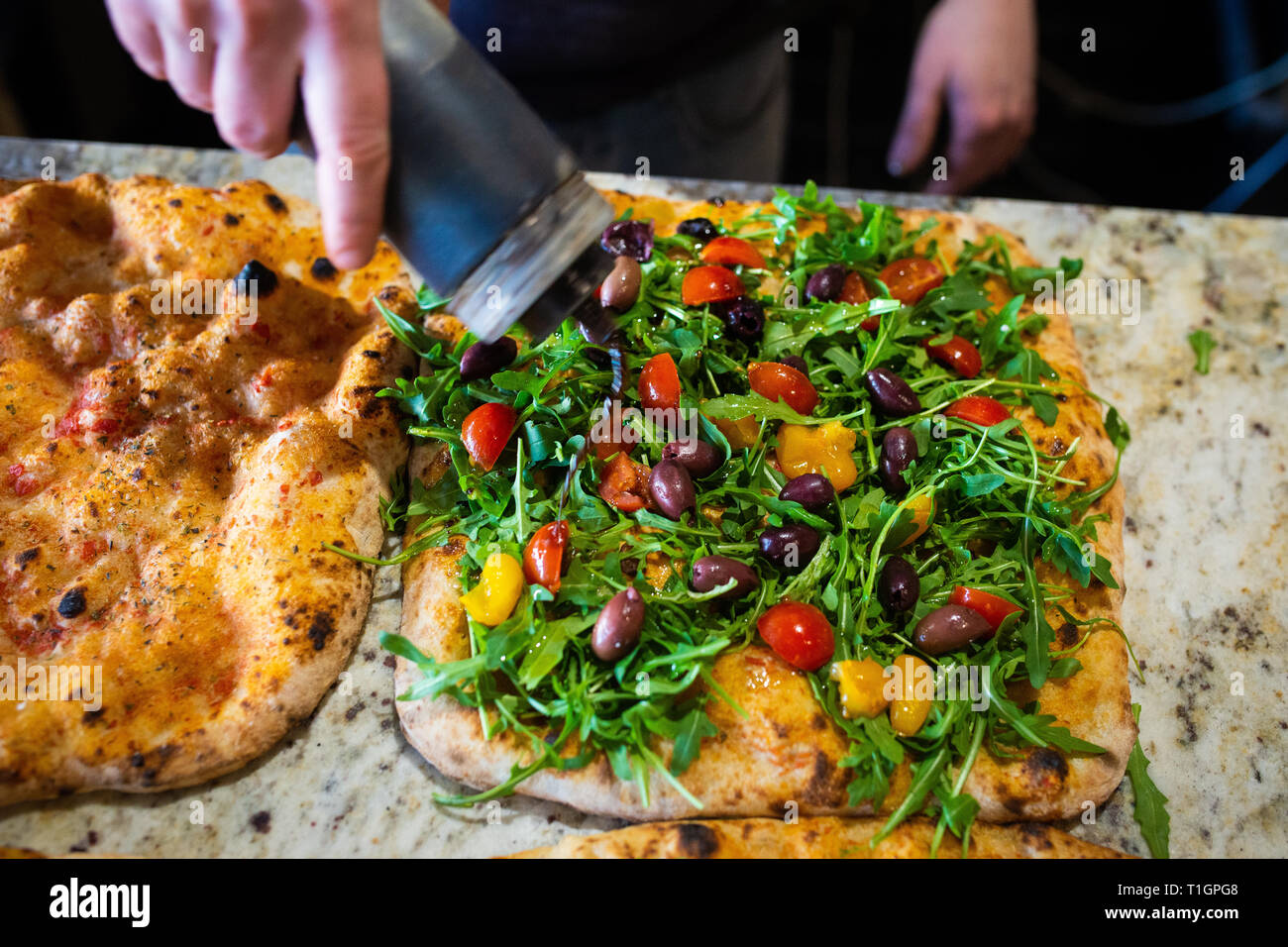 a chef man in an italian pizzeria preparing a colourful wood fired vegan pizza, drizzling with balsamic dressing Stock Photo