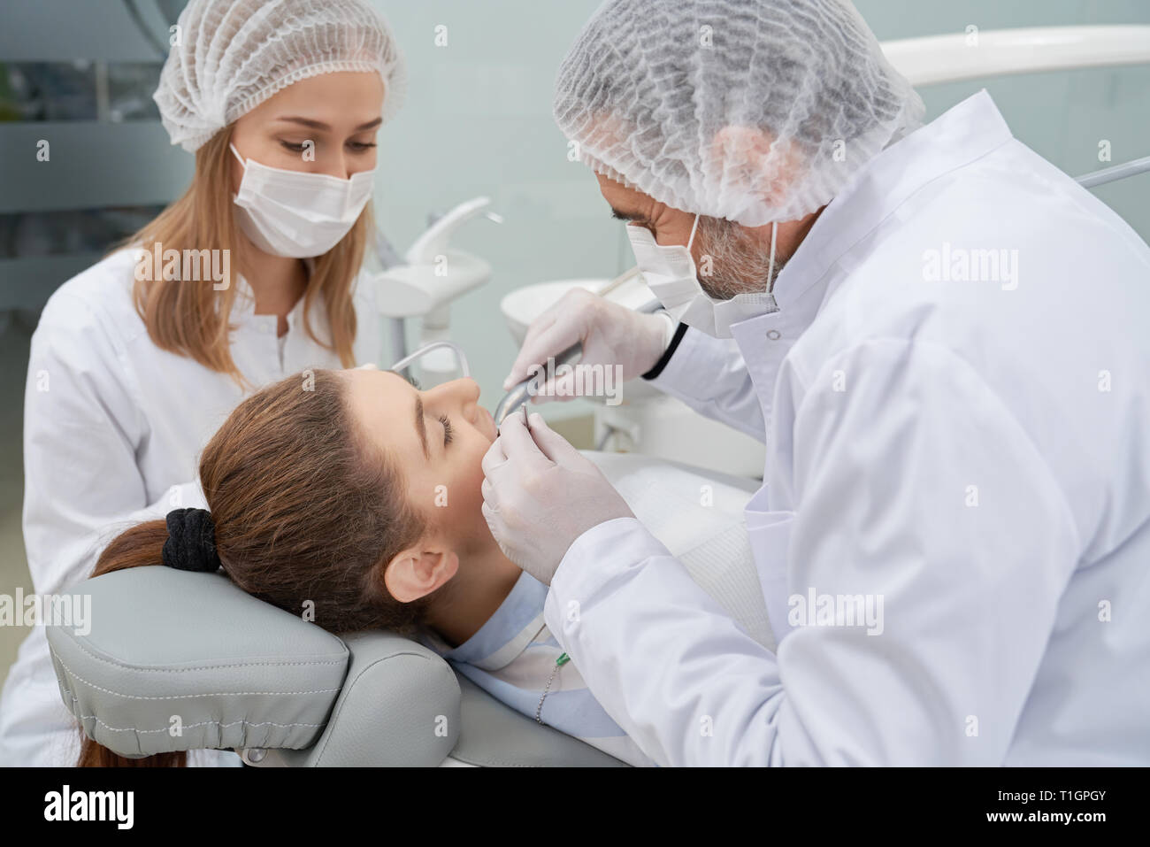 Professional doctor and assistant working with client in dentistry clinic. Woman lying on