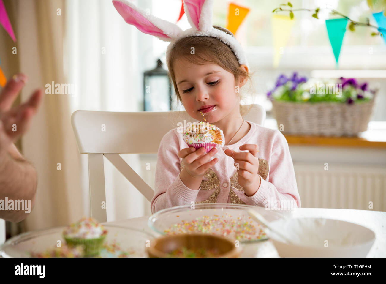 Father and daughter celebrating Easter, eating cupcakes covered with glaze. Happy family holiday. Cute little girl in bunny ears. Beautifully decorate Stock Photo