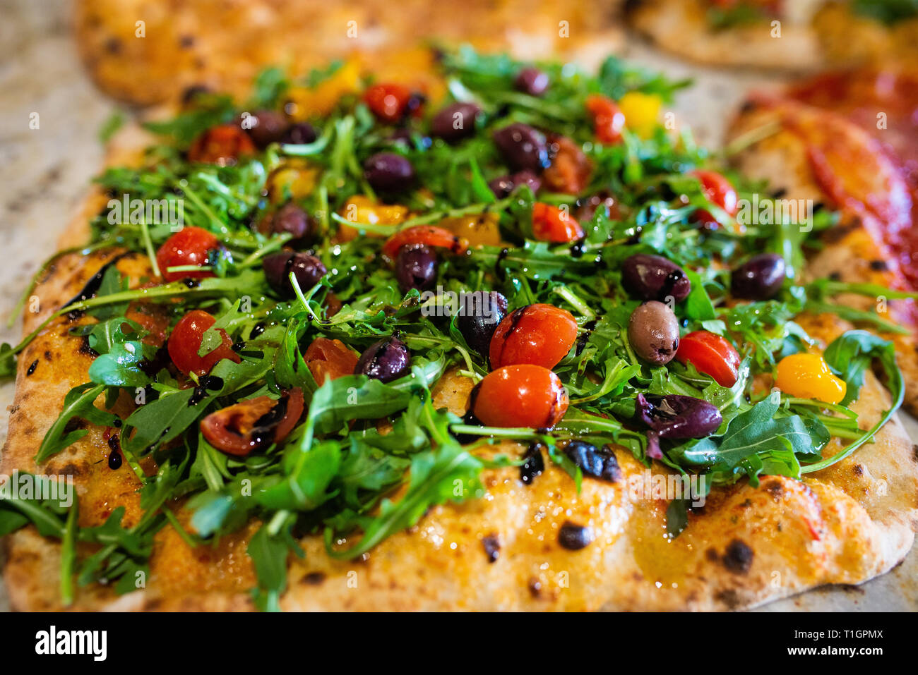 a colourful roman style Italian wood fired plant based vegan pizza in a trattoria/pizzeria, with olives tomatoes and rocket Stock Photo