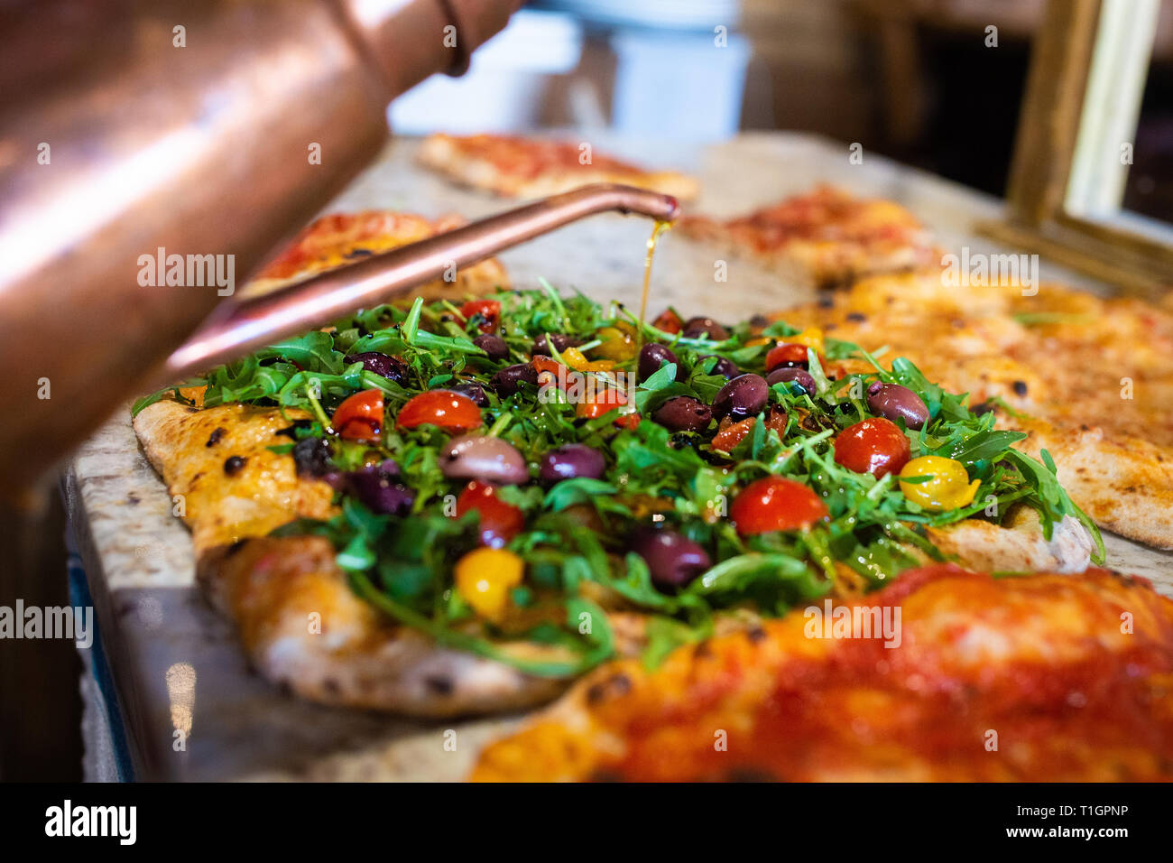 olive oil being drizzled onto an authentic roman style italian wood fired vegan pizza in a trattoria Stock Photo