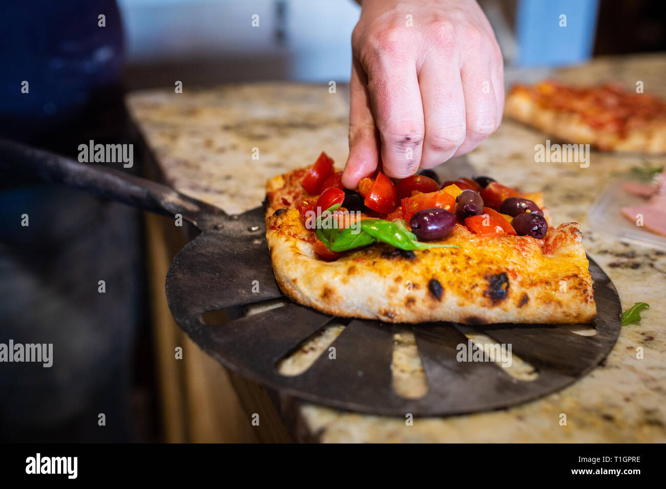 a chef man puts the final touches to a roman style italian pizza slice in a trattoria/pizzeria. Preparing pizza. Selective focus Stock Photo