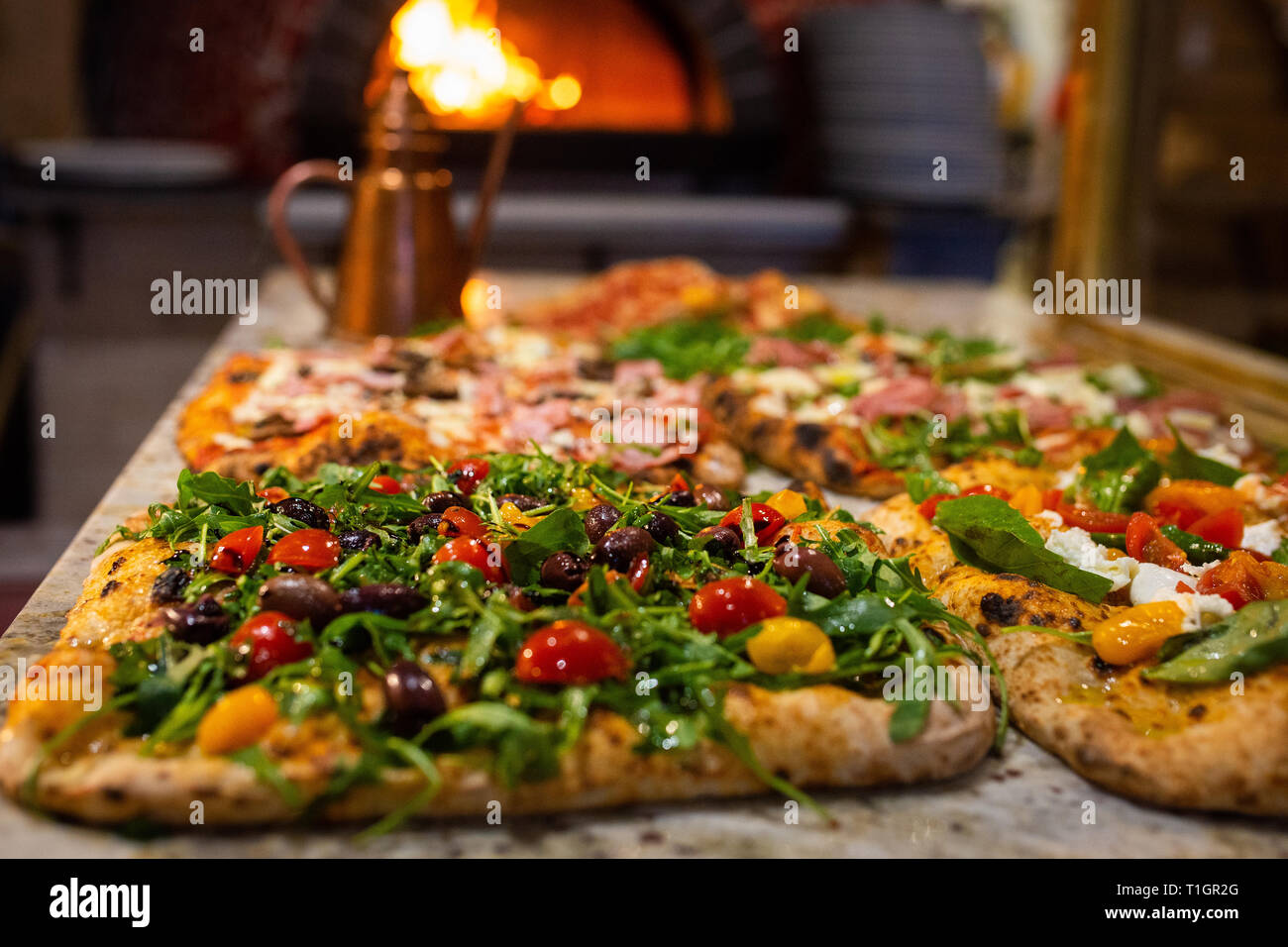colourful authentic roman style italian wood fired pizzas on counter in front of wood fire oven. In a trattoria/pizzeria/restaurant Stock Photo