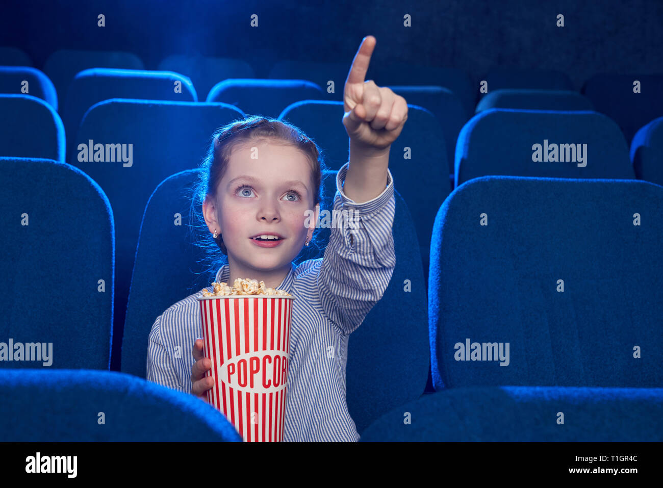 Beautiful little girl sitting in cinema theatre. Kid holding popcorn ...