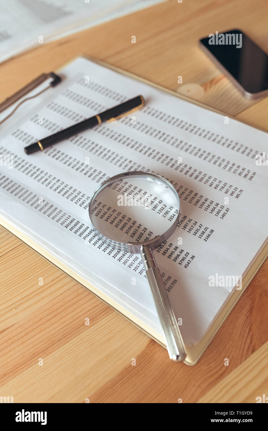 Business report analysis, magnifying glass over paper spreadsheet on office table Stock Photo