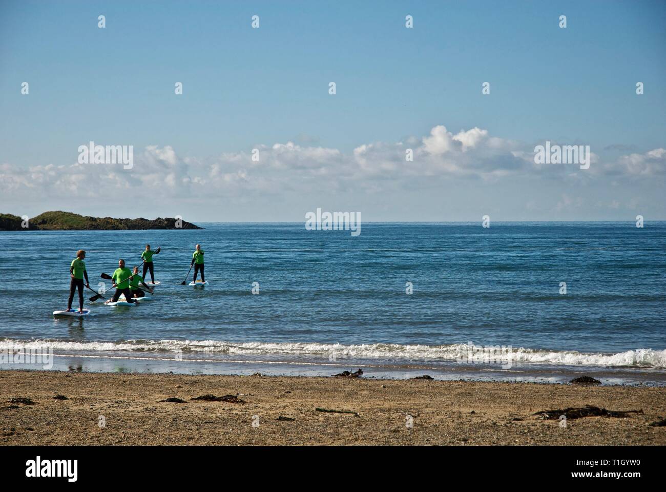 Distant figures approach the beach on paddle boards, Rhosneigr, Anglesey, North Wales, UK Stock Photo