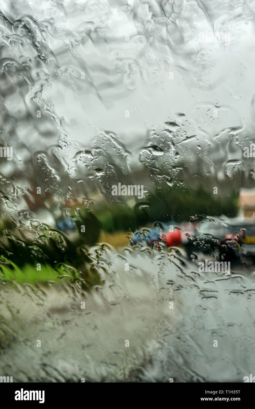 Rain on wet car windscreen with out of focus suburban residential street in background. Stock Photo