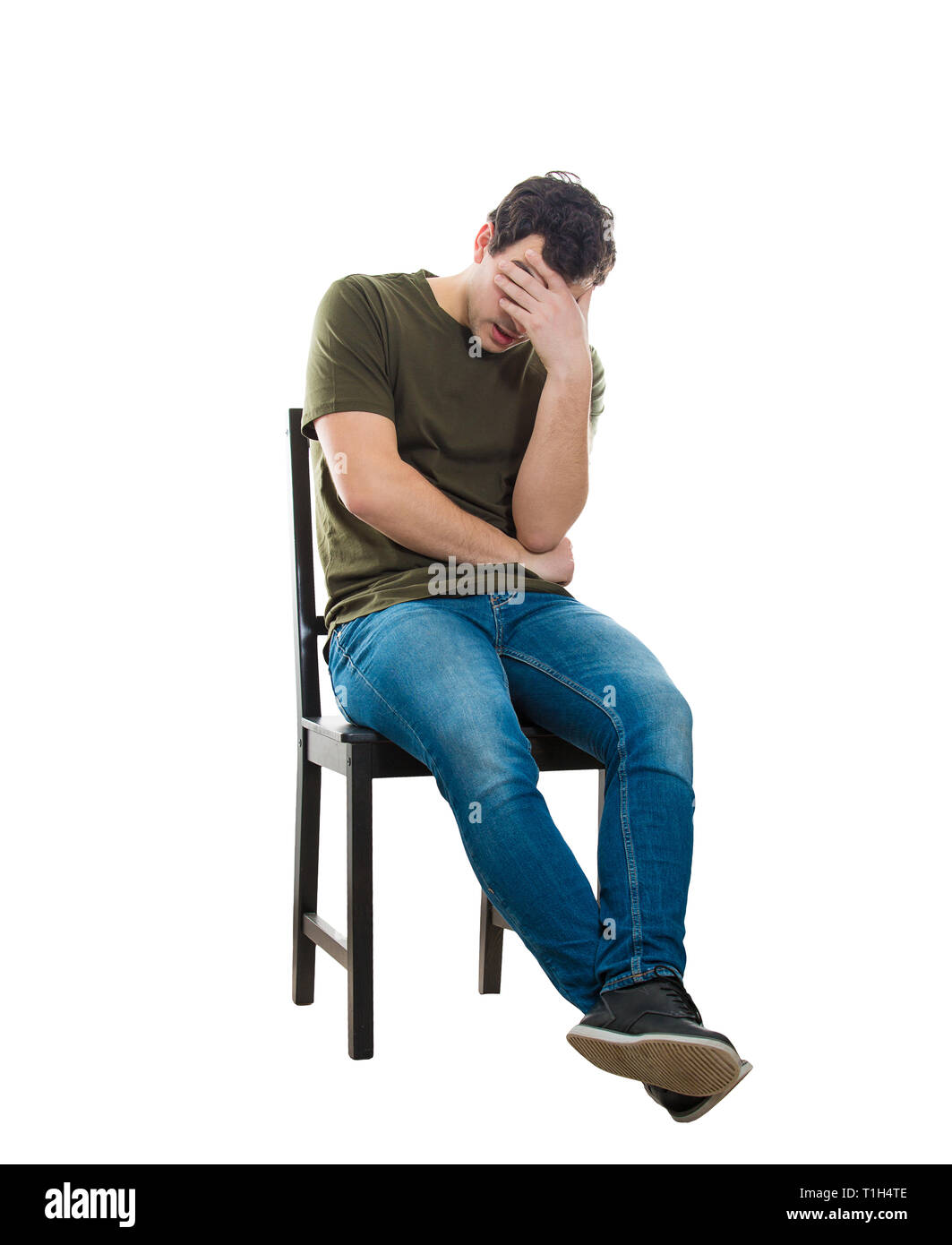 Sad and disappointed man sitting on a chair covering his face with hand, full length isolated over white background. Desperate casual guy having anxie Stock Photo