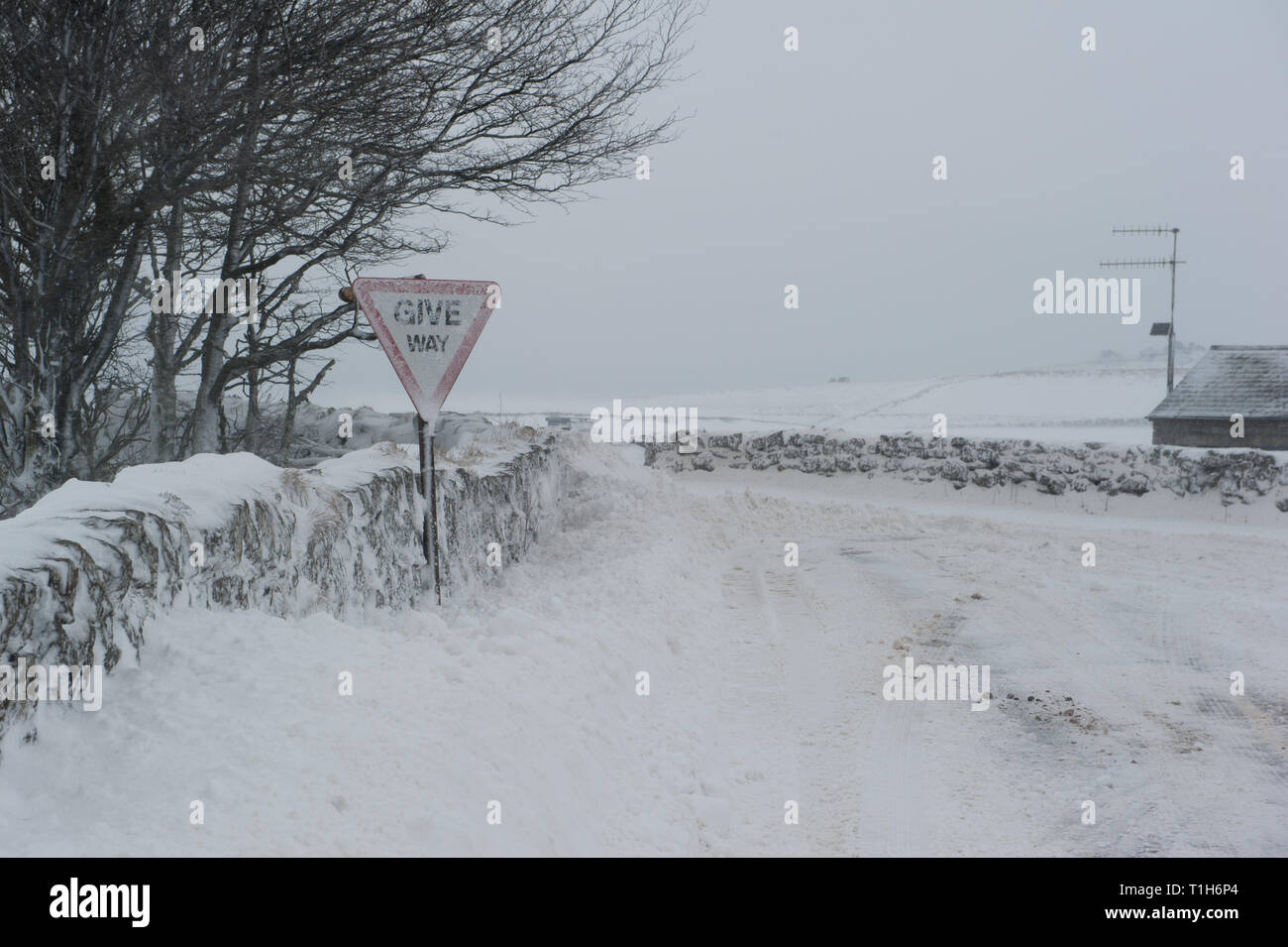 snow covered road junction in rural location, with give way warning sign covered in snow Stock Photo