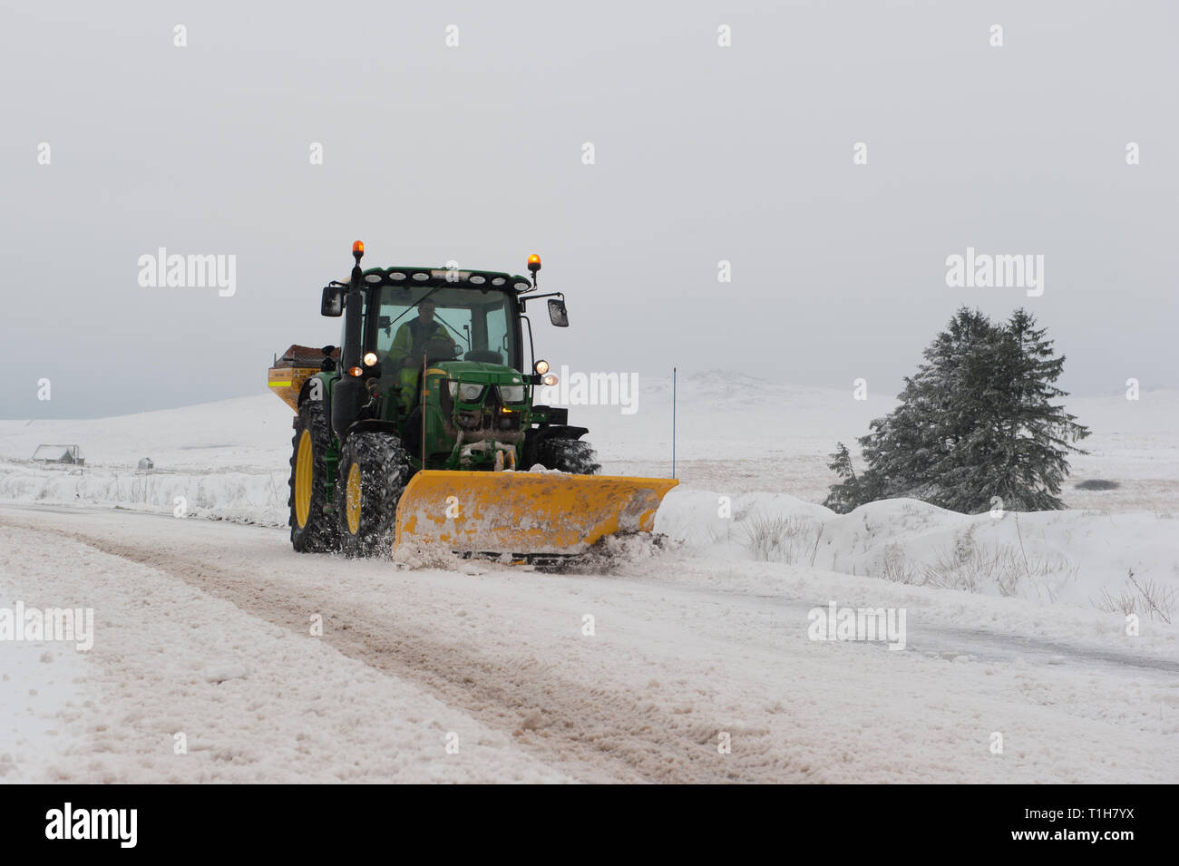 tractor fitted with snow plough clearing snow covered road on Dartmoor