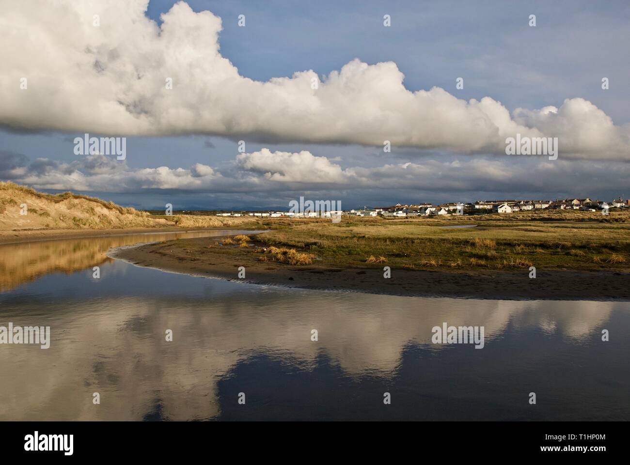 Blue sky and clouds reflected in the still waters of Afon Crigyll, with the village in the distance, Rhosneigr, Anglesey, North Wales, UK Stock Photo