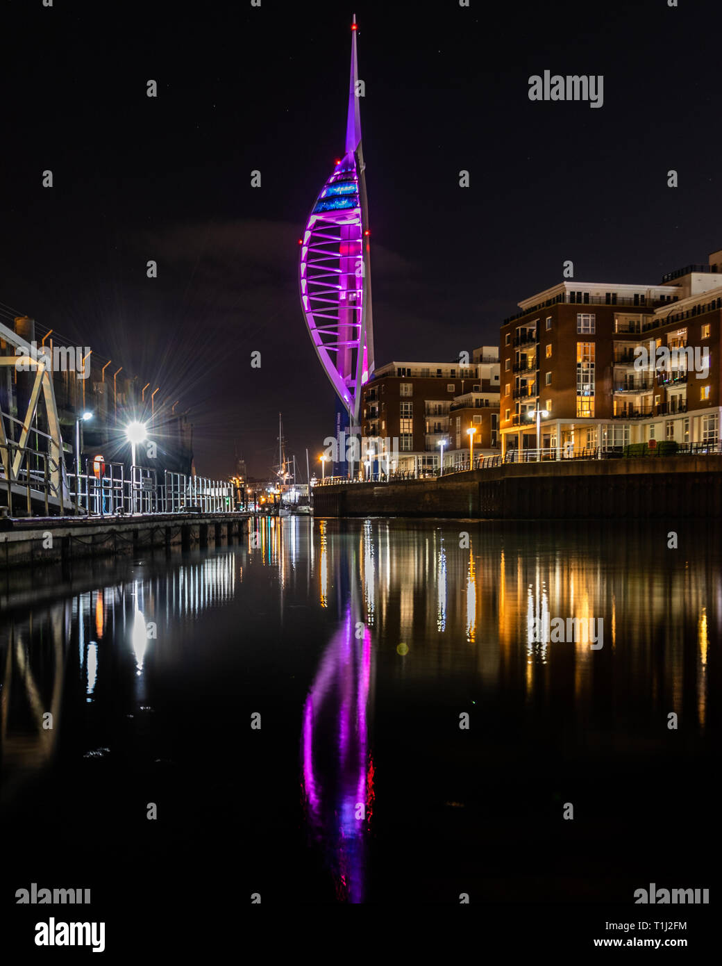 Spinnaker tower at Gunwharf Quays Portsmouth lit up purple at night for National Epilepsy Day reflecting on the water Stock Photo