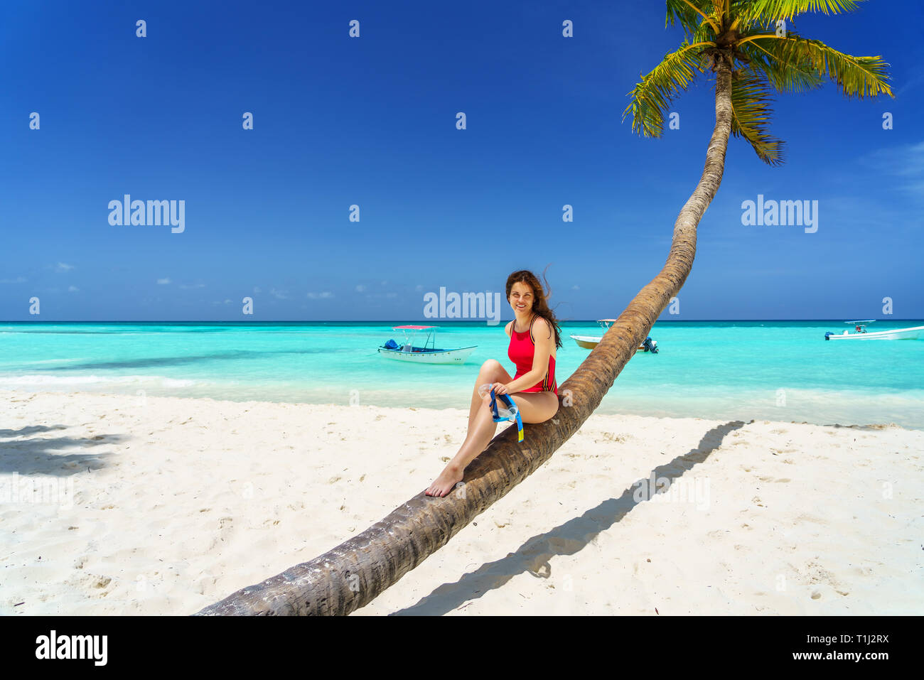 Young woman sitting on palm tree on the beach in Dominican Republic Stock Photo