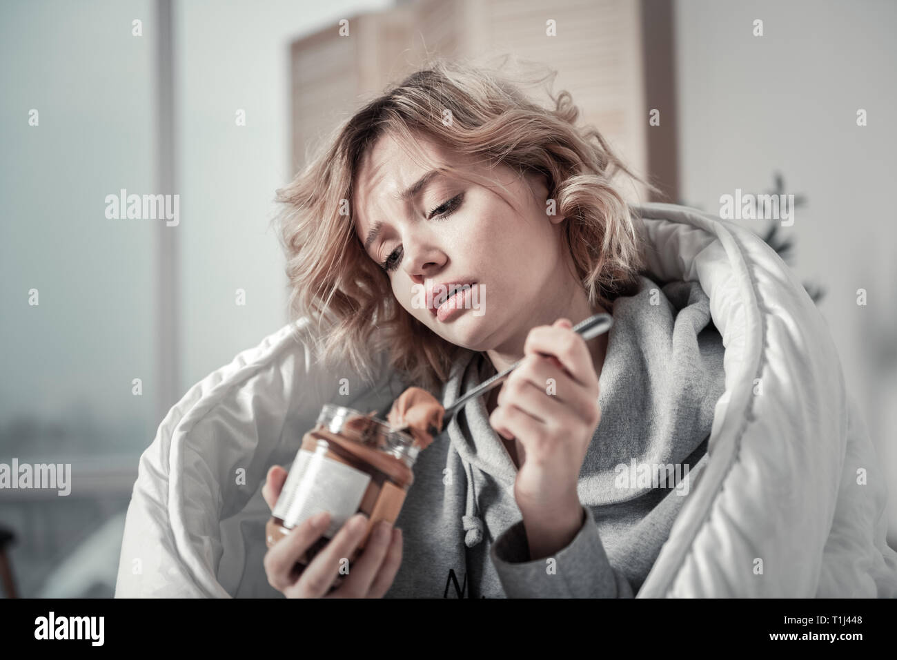 Young unhappy woman eating chocolate paste feeling stressed Stock Photo