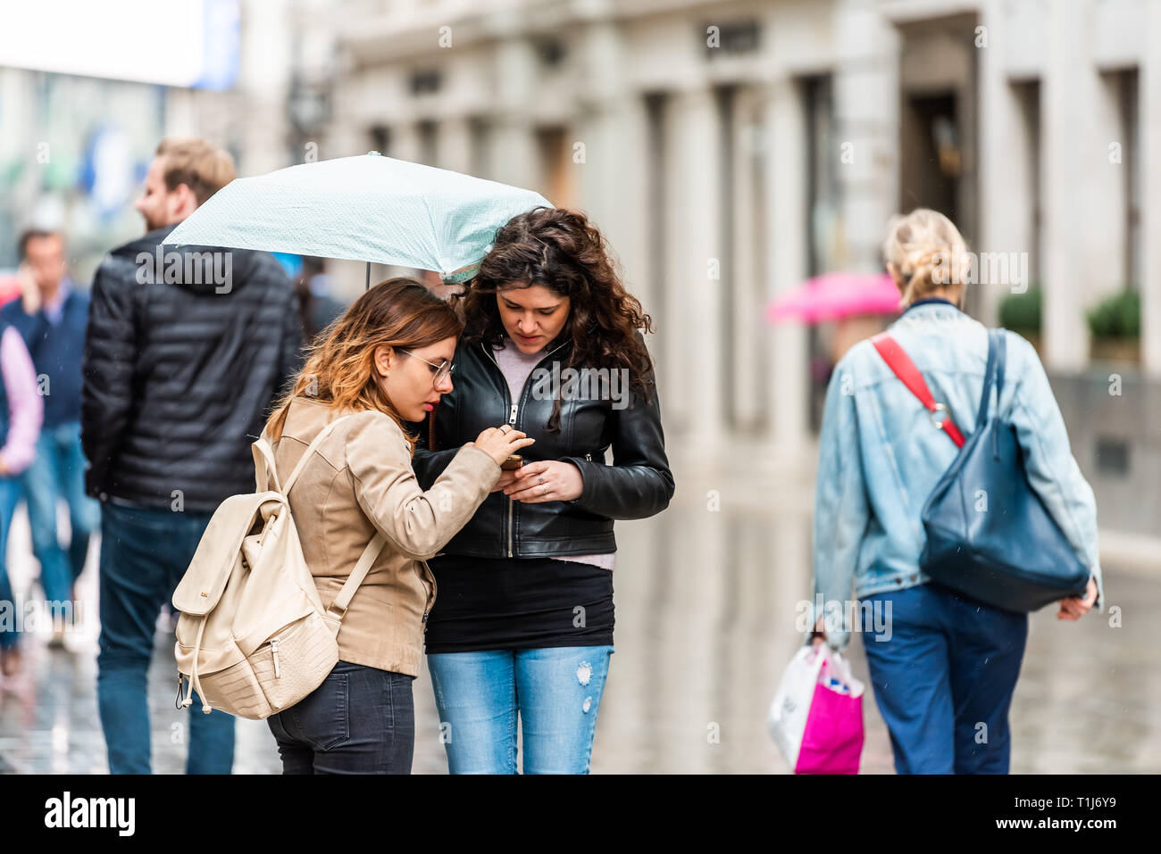 London, UK - September 12, 2018: Two women standing walking with umbrella in rainy city weather on sidewalk street wet road shopping in SoHo lost look Stock Photo