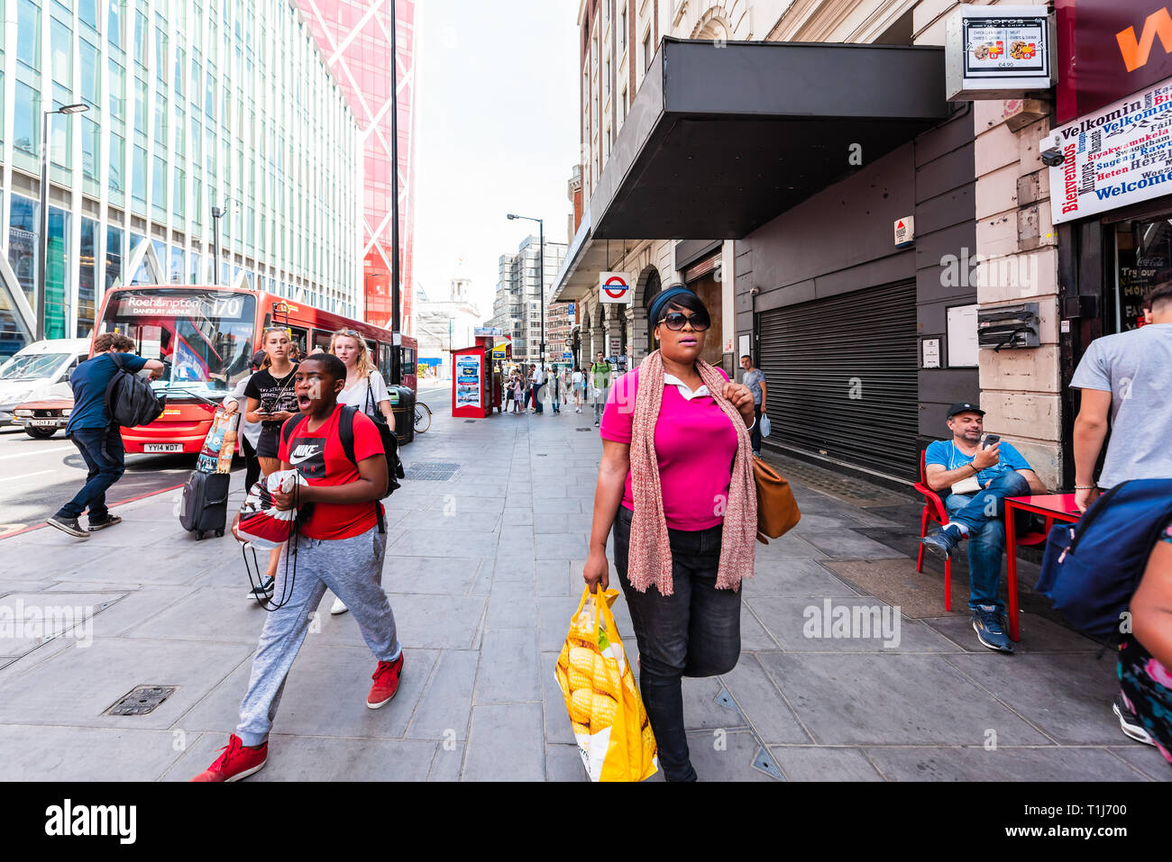 London, UK - June 24, 2018: Many people walking on sidewalk pavement street shopping by store retail during day in city crowded busy Stock Photo