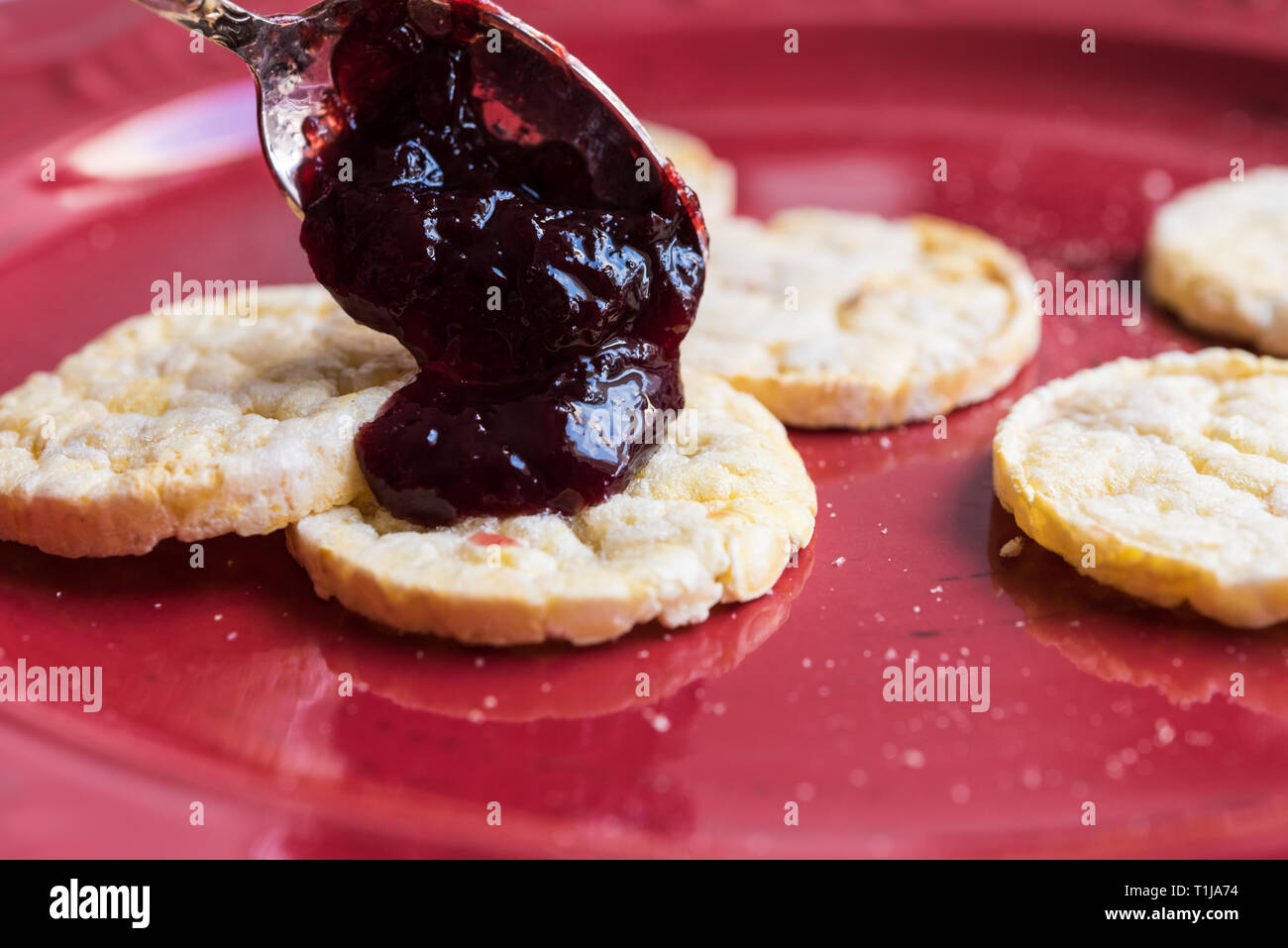 Eating plum jam on a red plate with corn / rice biscuits Stock Photo