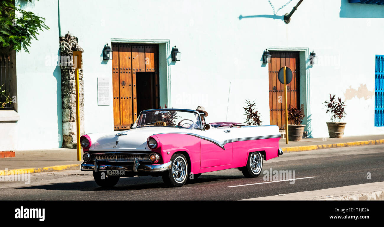 Havana, Cuba - 25 July 2018: A 1956 Ford Fairlane pink and white convertible taxi in Havana Cuba driving around looking for passengers. Stock Photo