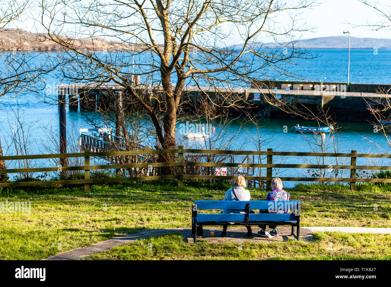 Schull, West Cork, Ireland. 27th March, 2019. Two ladies enjoy the view of Schull Harbour at the end of a beautiful day in West Cork. The remainder of the day will be sunny with highs of 12° Celsius. Credit: Andy Gibson/Alamy Live News. Stock Photo