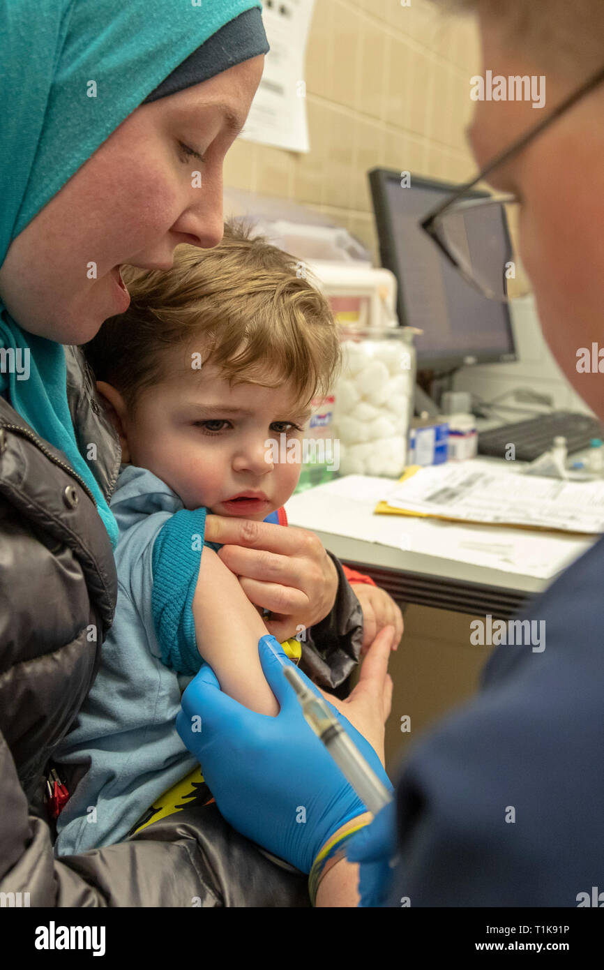 Southfield, Michigan, USA. 27th Mar, 2019. Adam Almahariq, 2, gets the MMR vaccine at the Oakland County Health Department to protect him against a measles outbreak. Twenty-two measles cases have been confirmed in the area since the visit of an infected traveler from Israel. Miranda Almahariq holds her son as nurse Jayne DeBoer-Rowse administers the shot. Credit: Jim West/Alamy Live News Stock Photo