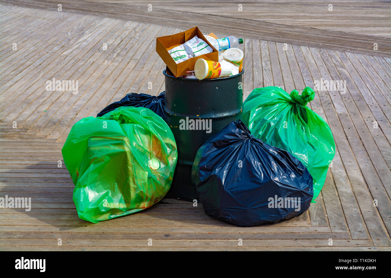 Pile of garbage bags near the overfilled garbage bin on the boardwalk