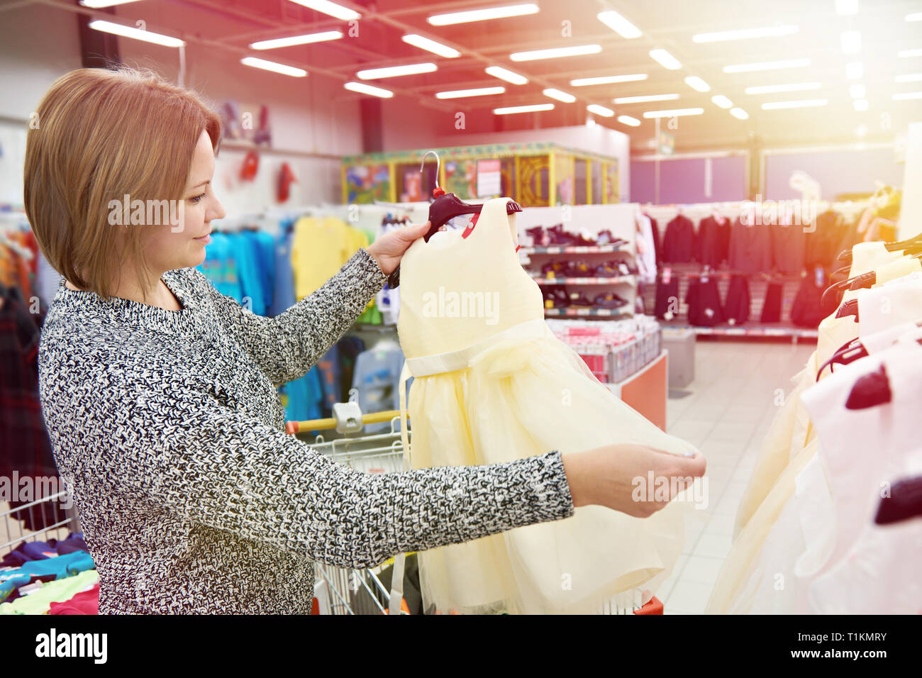 Woman chooses a dress for little daughter in the store Stock Photo