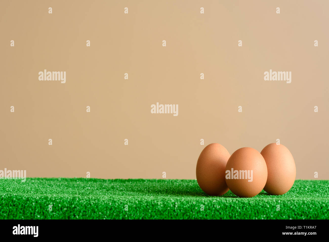 Three organic eggs, on a green grass surface, with a brown background. Easter concept. Stock Photo