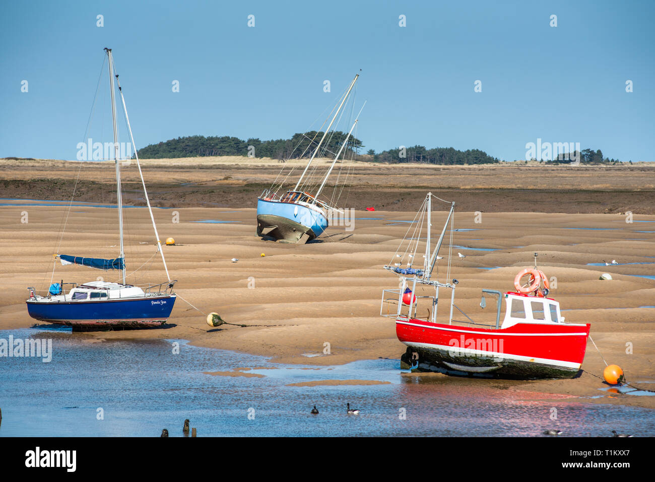 Colourful boats marooned on sandbanks at low tide on East Fleet river estuary at Wells next the sea, North Norfolk coast, East Anglia, England, UK. Stock Photo