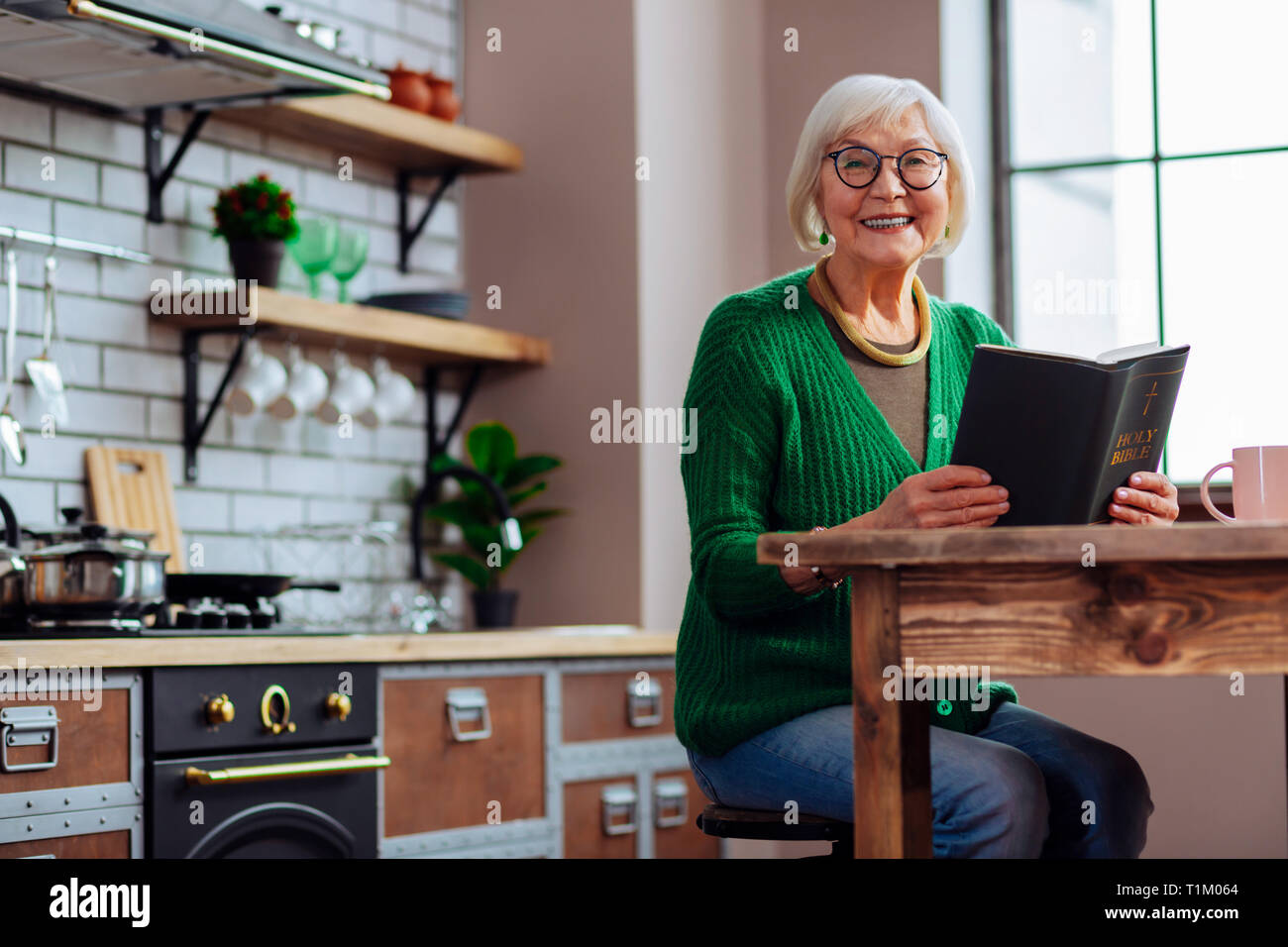 Smiling female happily keeping book in hands at kitchen room Stock Photo