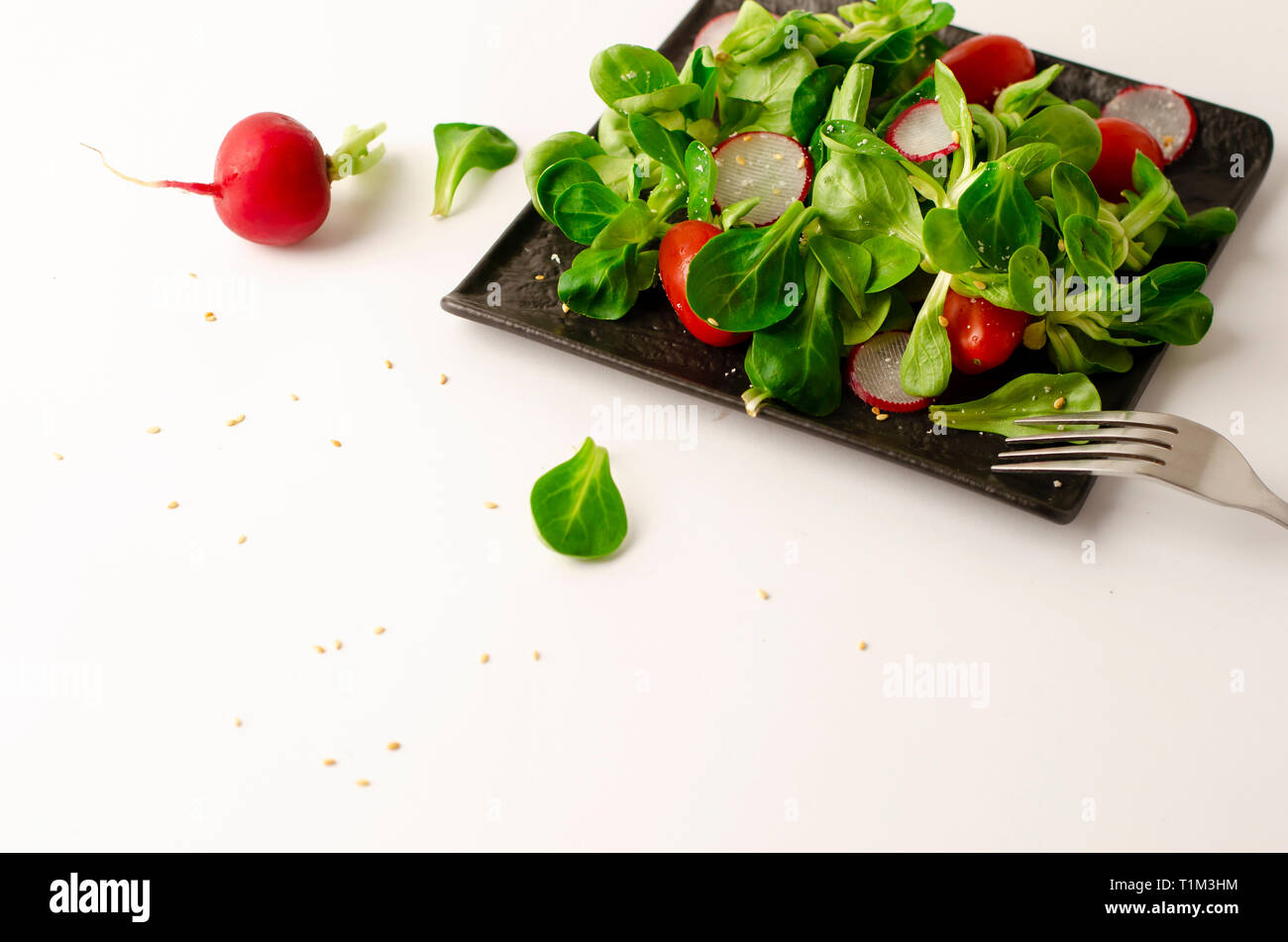 Healthy breakfast or lunch. Fresh vegetable salad of radish, tomatoes and corn salad or Valerianella locusta. Close up on black plate. Diet and vegeta Stock Photo