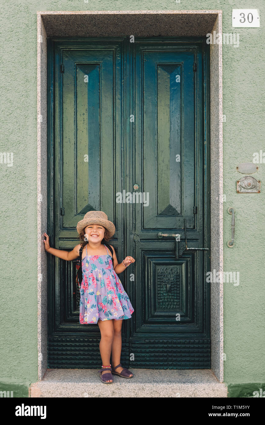 Little girl poses funny and smiling in front of the green door of the ...