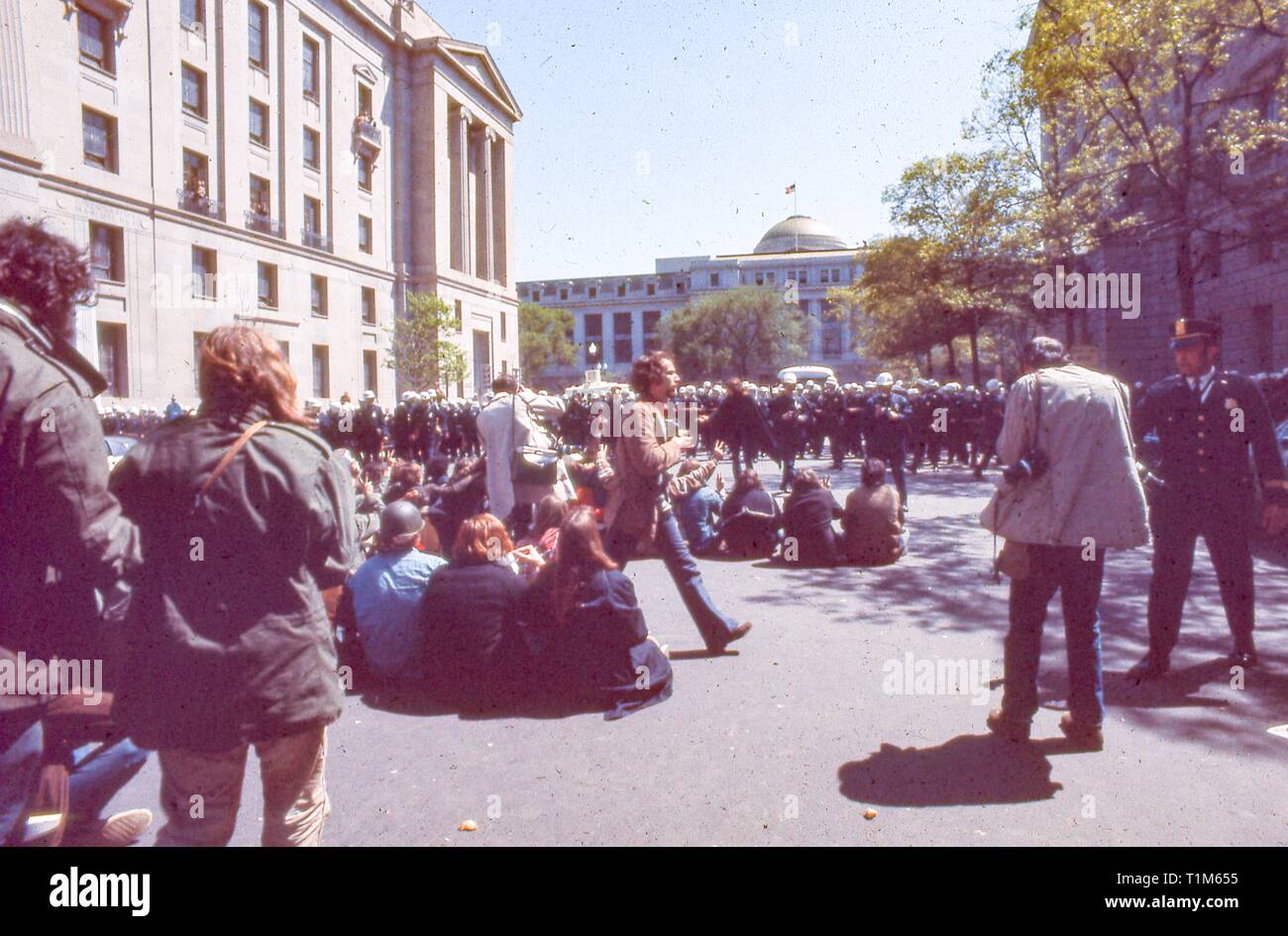 During the 1971 May Day Protests against the Vietnam War, protesters in hippie attire sit in the middle of 10th St NW, on a sunny day, facing a large number of police officers, in Washington, DC, May 1971. () Stock Photo