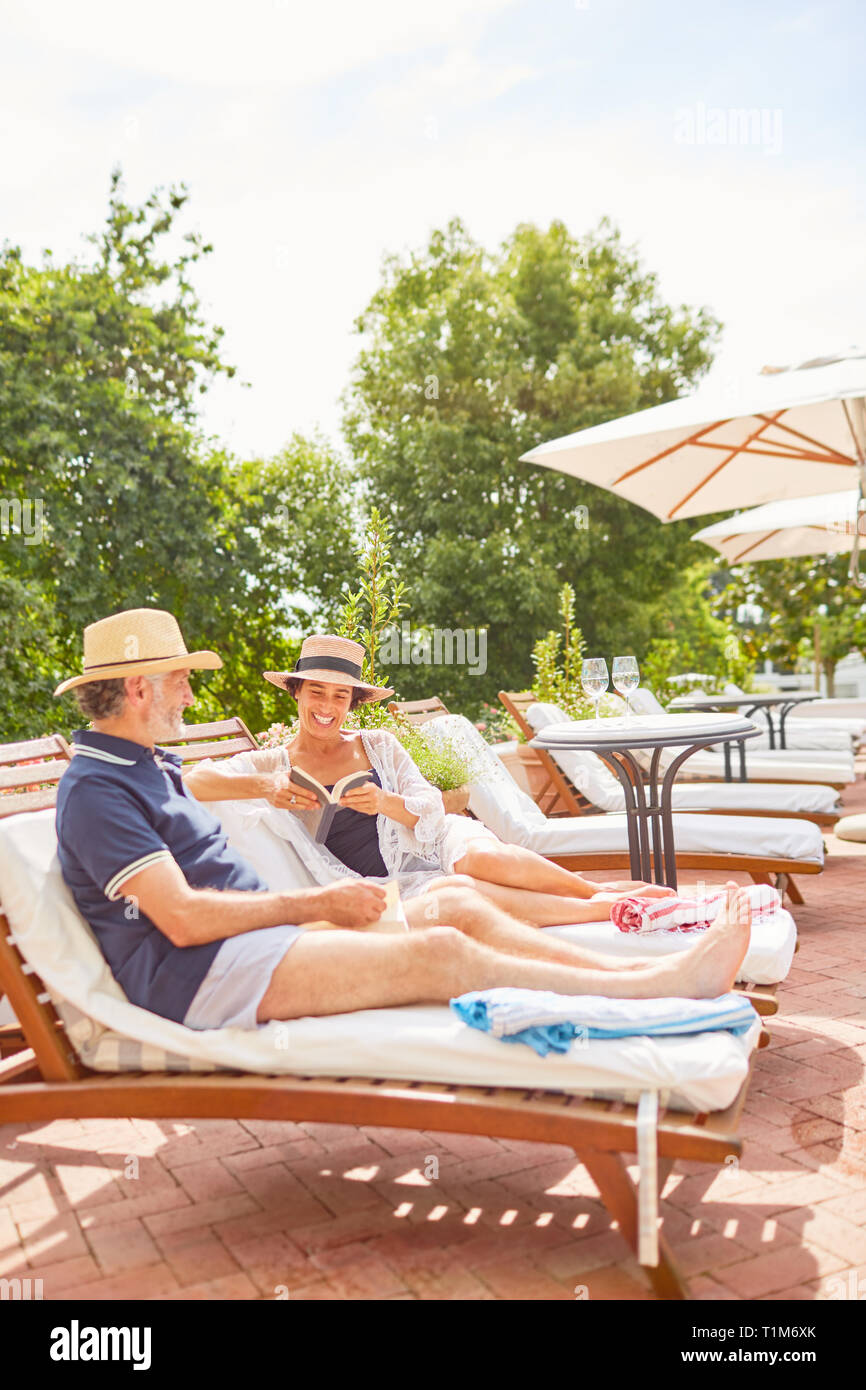Mature couple relaxing, reading on lounge chairs at sunny resort poolside Stock Photo